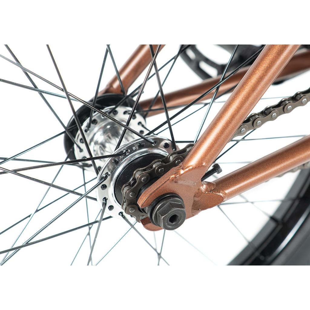 Close-up of a Colony Prody Elite 20 Inch Bike’s rear wheel, featuring metal spokes, chain, hub, and a bronze CrMo frame set against a white background.