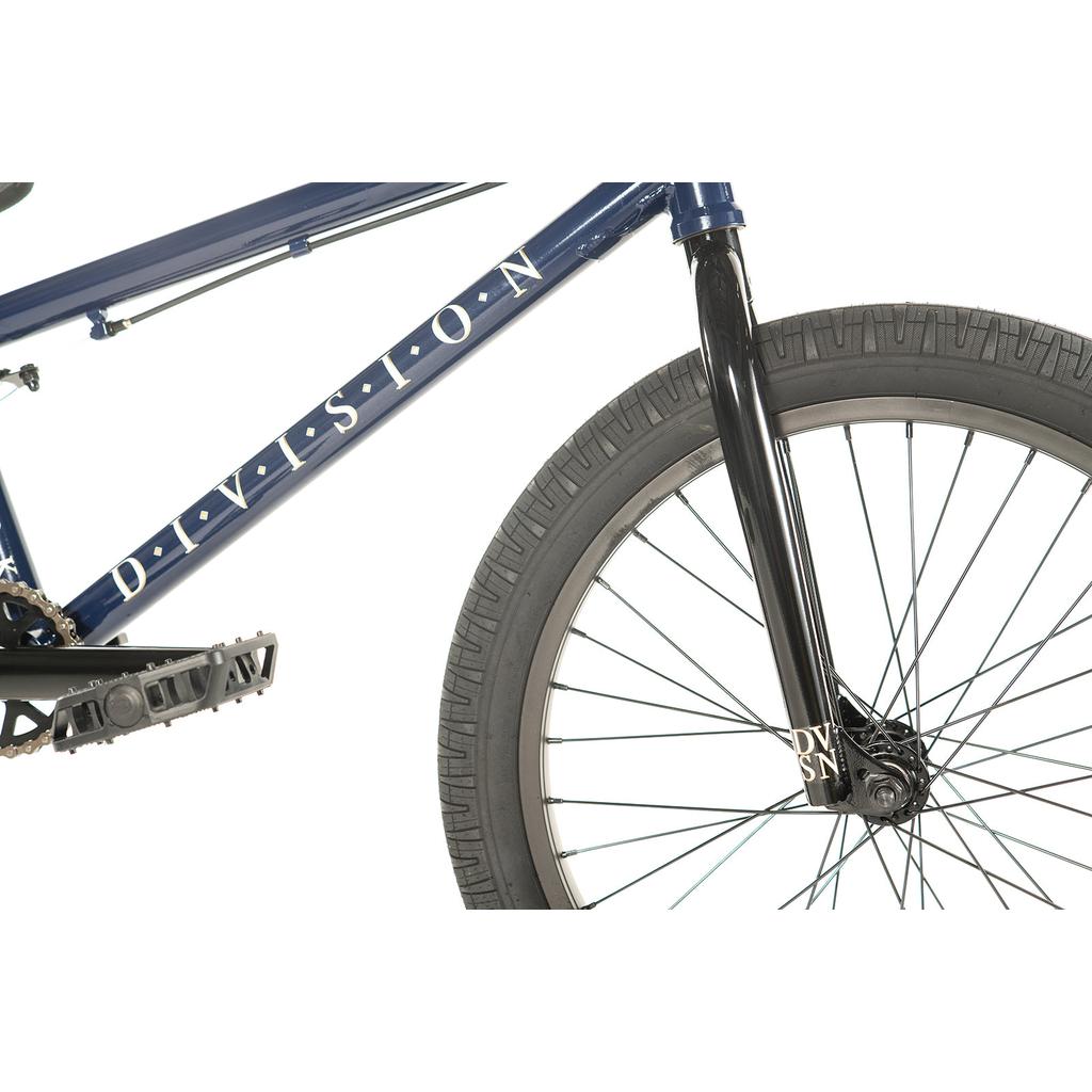 Close-up of the Division Reark 20 Inch Bike shows the blue frame labeled "DIVISION," front tire, black fork, and pedal against a white background. Features include a sealed bottom bracket and durable 3-piece cranks.
