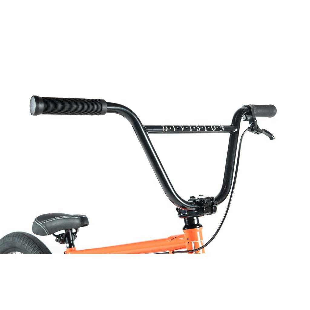 Close-up of black BMX-style handlebars and brake lever on the Division Reark 20 Inch Bike, with part of the seat and rear wheel visible. Features Hi-Tensile steel construction in an orange color.