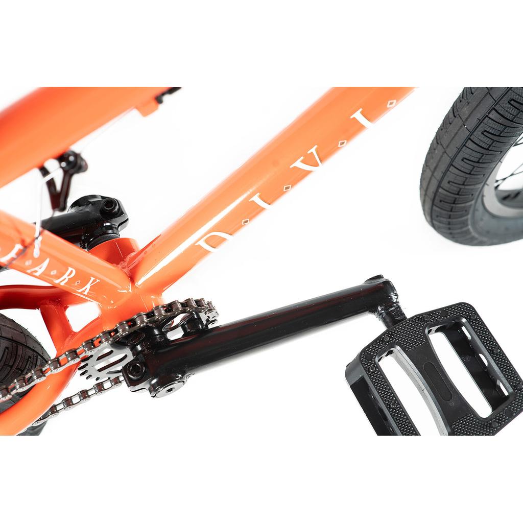 Close-up of the Division Reark 20 Inch Bike's Hi-Tensile steel crank, pedal, chain, and orange frame with partially visible "DIVI" text on a white background.