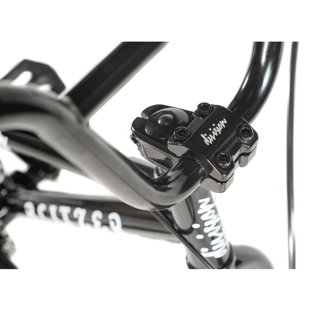 Close-up of the Division Blitzer 14 Inch Bike’s black handlebars and stem, showcasing the “division” logo and part of the youth bike’s frame with 14-inch wheels in the background.