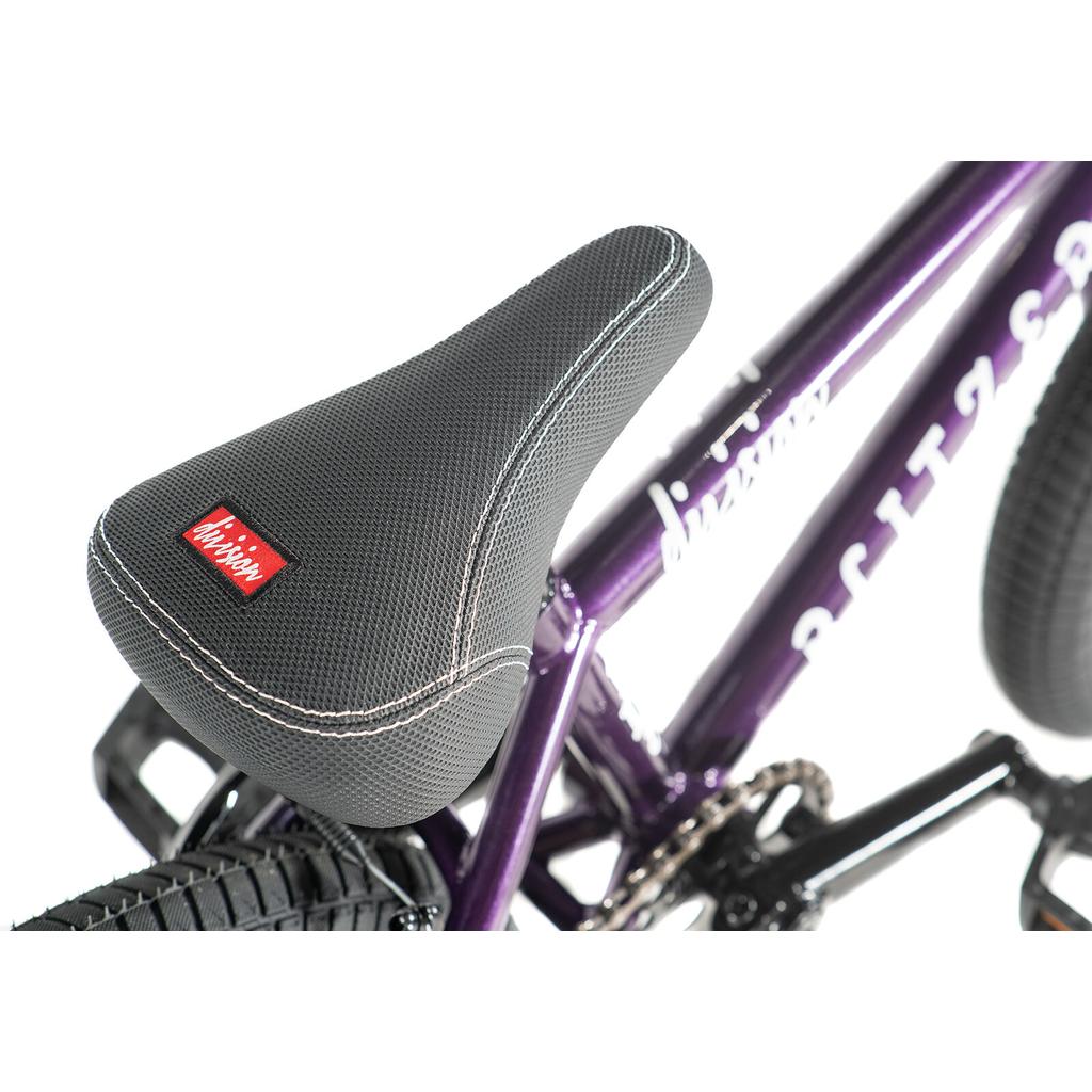 Close-up of a textured black bicycle seat with white stitching on a purple Division Blitzer 14 Inch Bike frame, featuring a red "Mission" label.