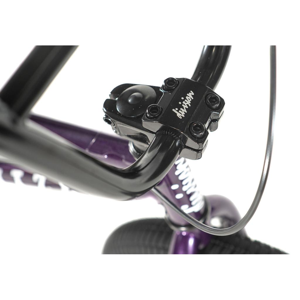 Close-up of the Division Blitzer 18 Inch Bike's black BMX handlebar and stem with “invision” text, attached to a purple Hi-Ten frame and a visible black front tire.