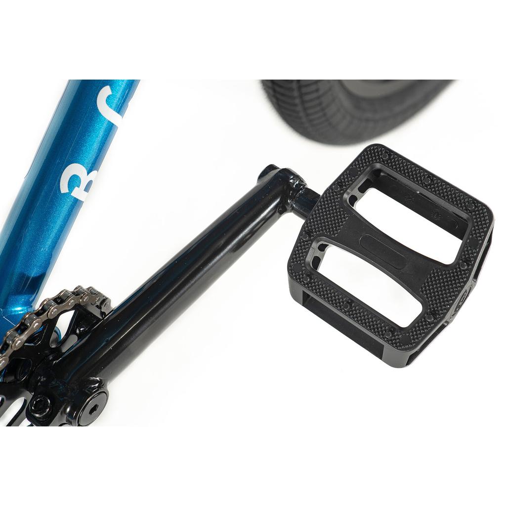 Close-up of a black pedal attached to the crank arm of the Division Blitzer 20 Inch Bike, with part of the BMX frame and 20” wheels visible in the background.