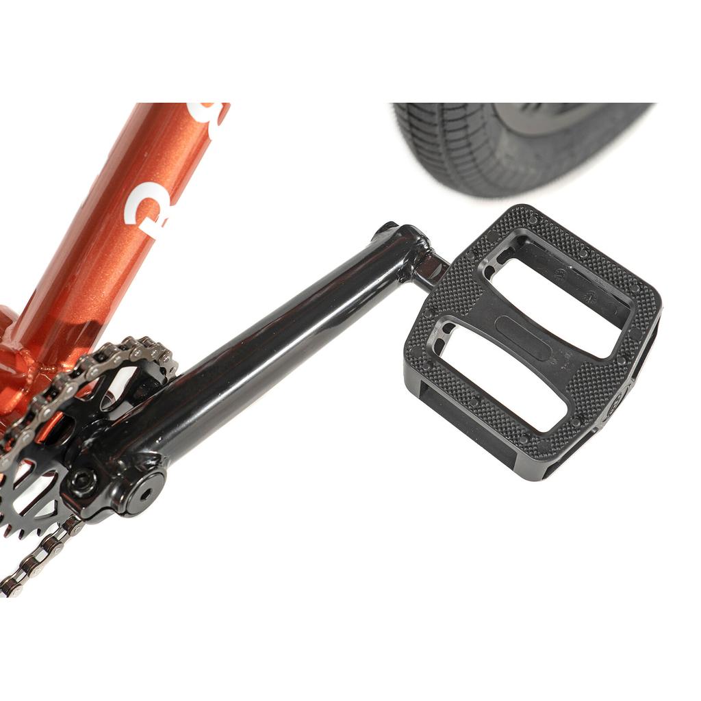 Close-up of a black pedal and 3-piece cranks on the Division Reark 20 Inch Bike, featuring a red Hi-Tensile steel frame with the chain and rear wheel partially visible.