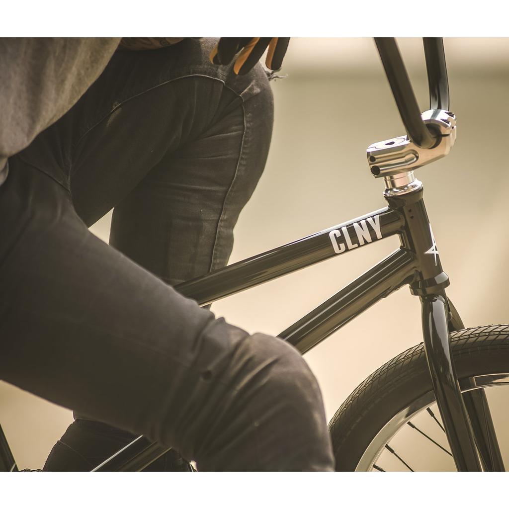 Close-up of a person in dark pants sitting on a black bicycle with "CLNY" on the frame, featuring the Colony Squareback Stem.