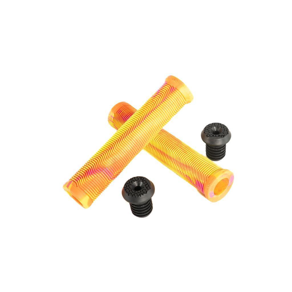 Two Colony Much Room Flangeless Grips in yellow and pink stripes are crossed, crafted from durable Krayton Rubber, with two black BMX bar ends placed beside them on a white background.