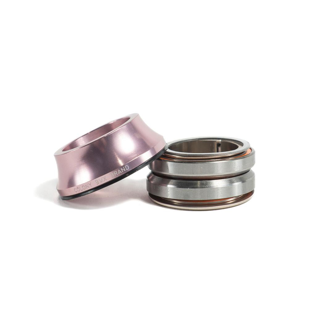 A Colony Tall Headset in pink top cap rests beside a silver 45/45 style bicycle bearing assembly, displayed on a white surface.