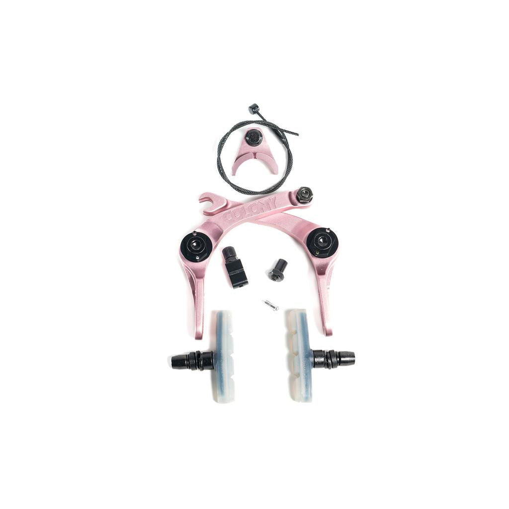 A disassembled Colony Brethren Brakes pink front caliper set with mounting hardware, brake pads, cable, and small components arranged on a white background for superior braking performance.