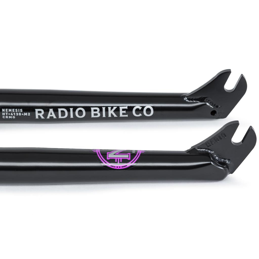 Close-up view of two black Radio Nemesis Forks dropouts, showcasing "RADIO BIKE CO" and "NEMESIS" branding in white and purple accents, crafted from heat-treated chromoly for a responsive ride.