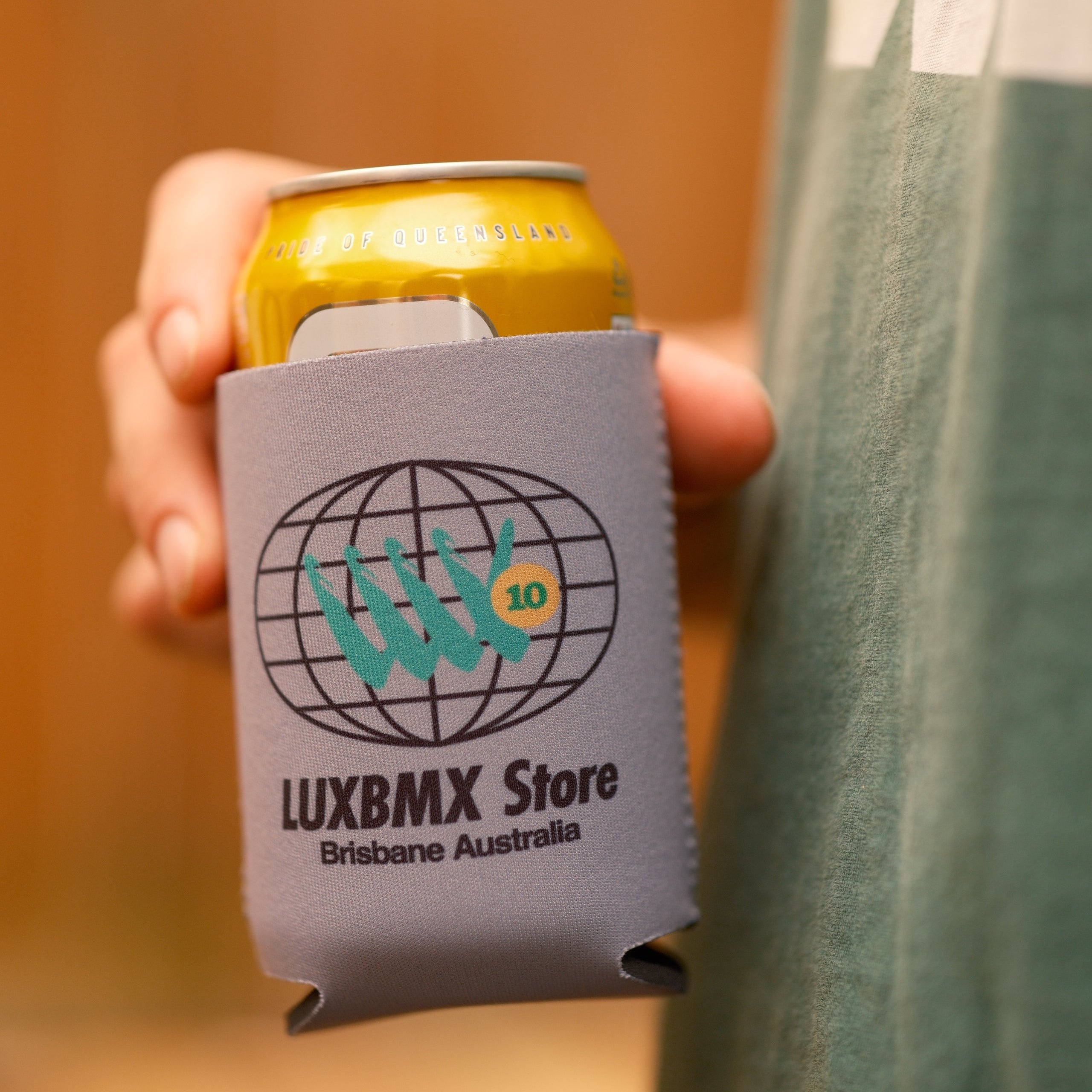 A person holds a can in the LUXBMX Stubby Cooler / 88, featuring the LUXBMX Store Brisbane Australia logo and a stylized BMX graphic, providing effective drink insulation.