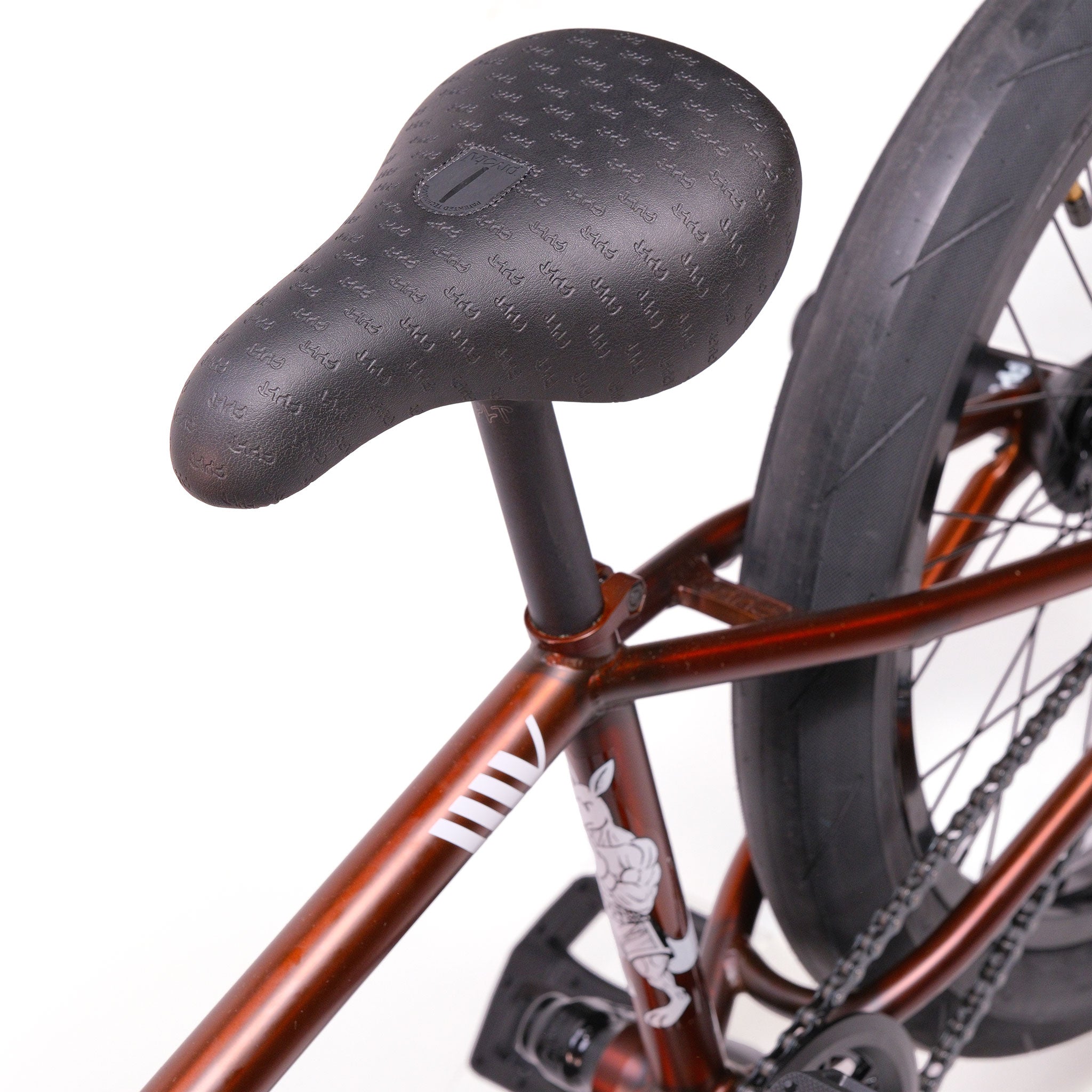 Close-up of a black seat on a brown Cult Dak X Eclat Custom 'Pat Freyne Signature' BMX bike, with part of the rear wheel and chain visible.