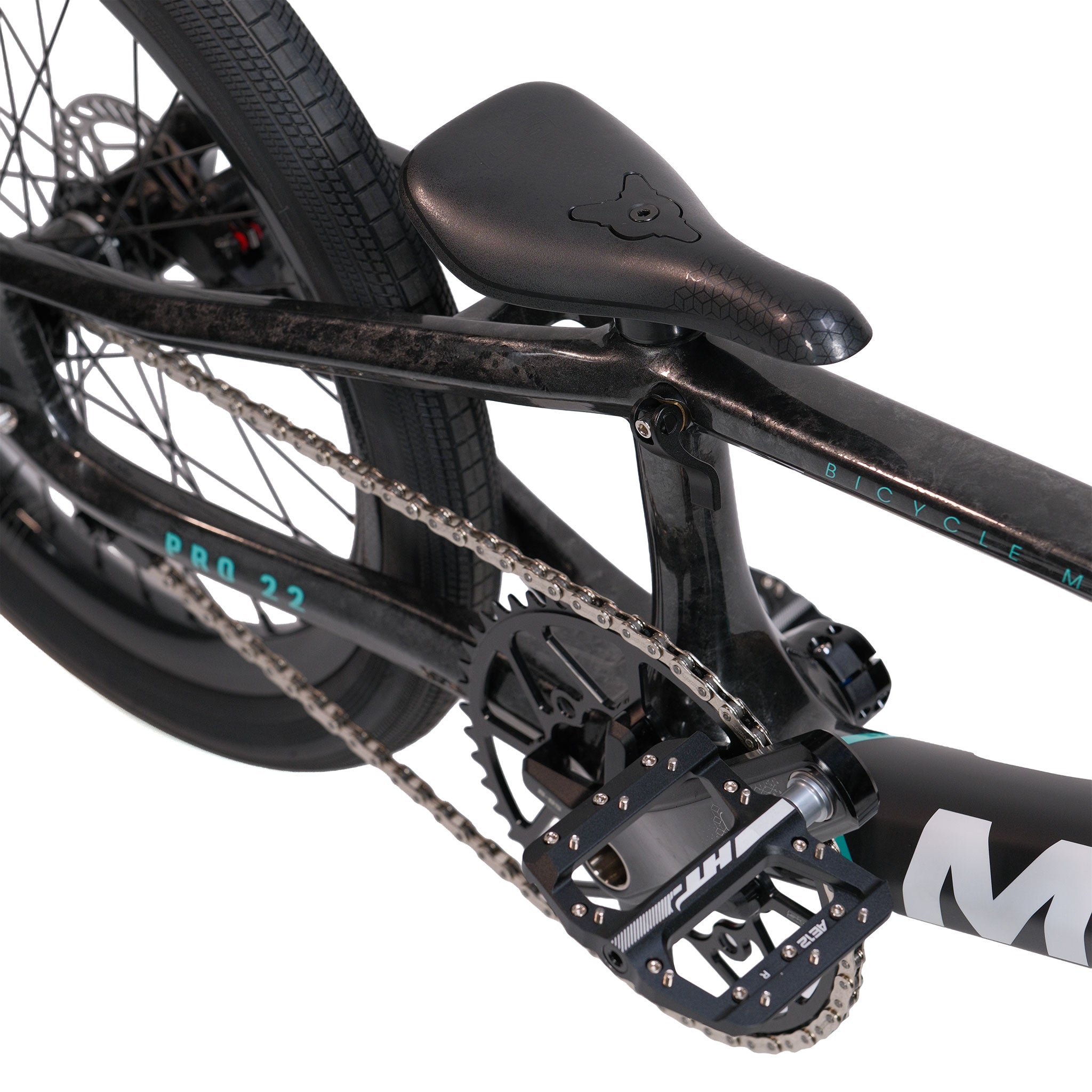 Close-up view of the Meybo HSX Carbon Pro XXL Race Bike's black saddle, pedal, chain, and rear wheel, highlighting essential BMX parts along with the carbon frame and drivetrain components.