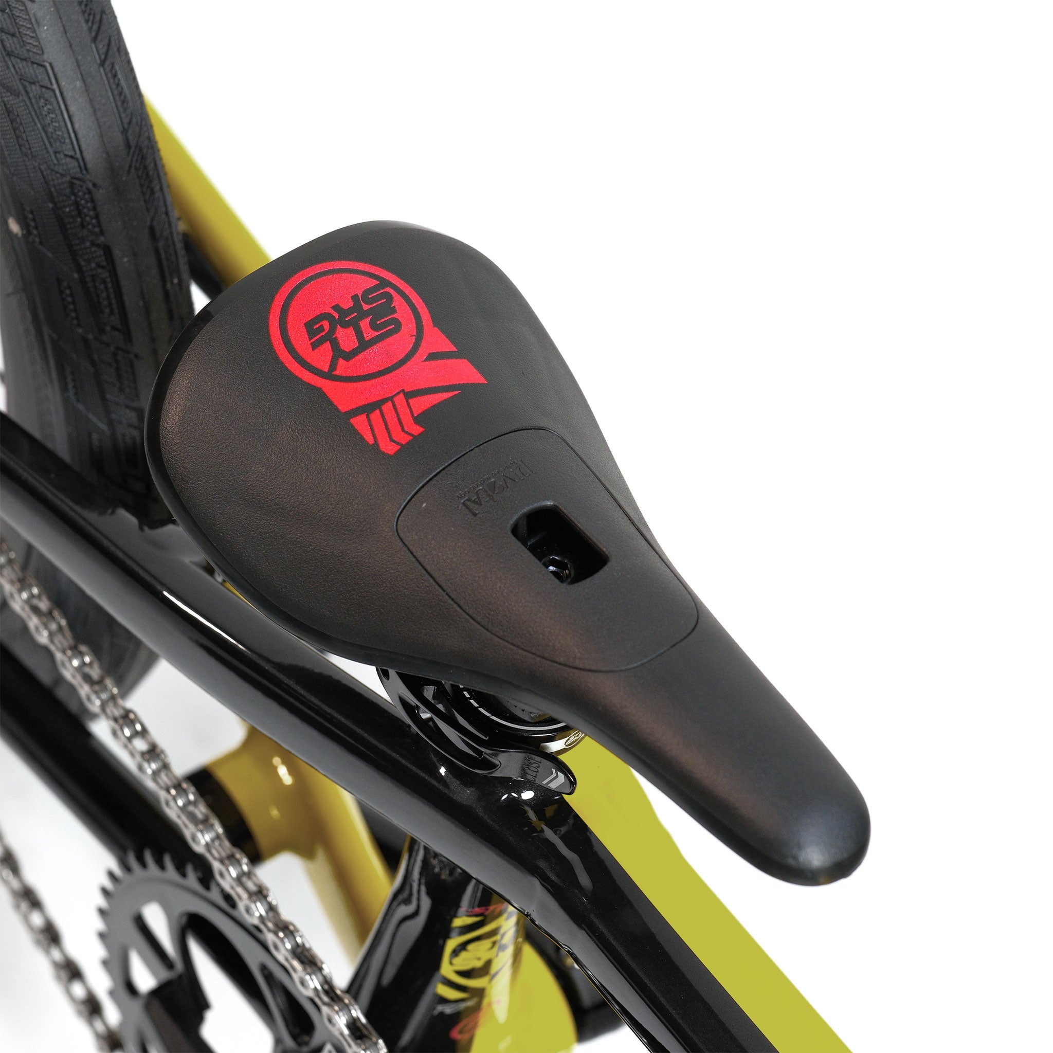 Close-up of the Stay Strong V5.1 Pro XXXL Race Bike’s black saddle with red graphics, mounted on its durable aluminium frame—showing the chain, tire, and part of the crankset.