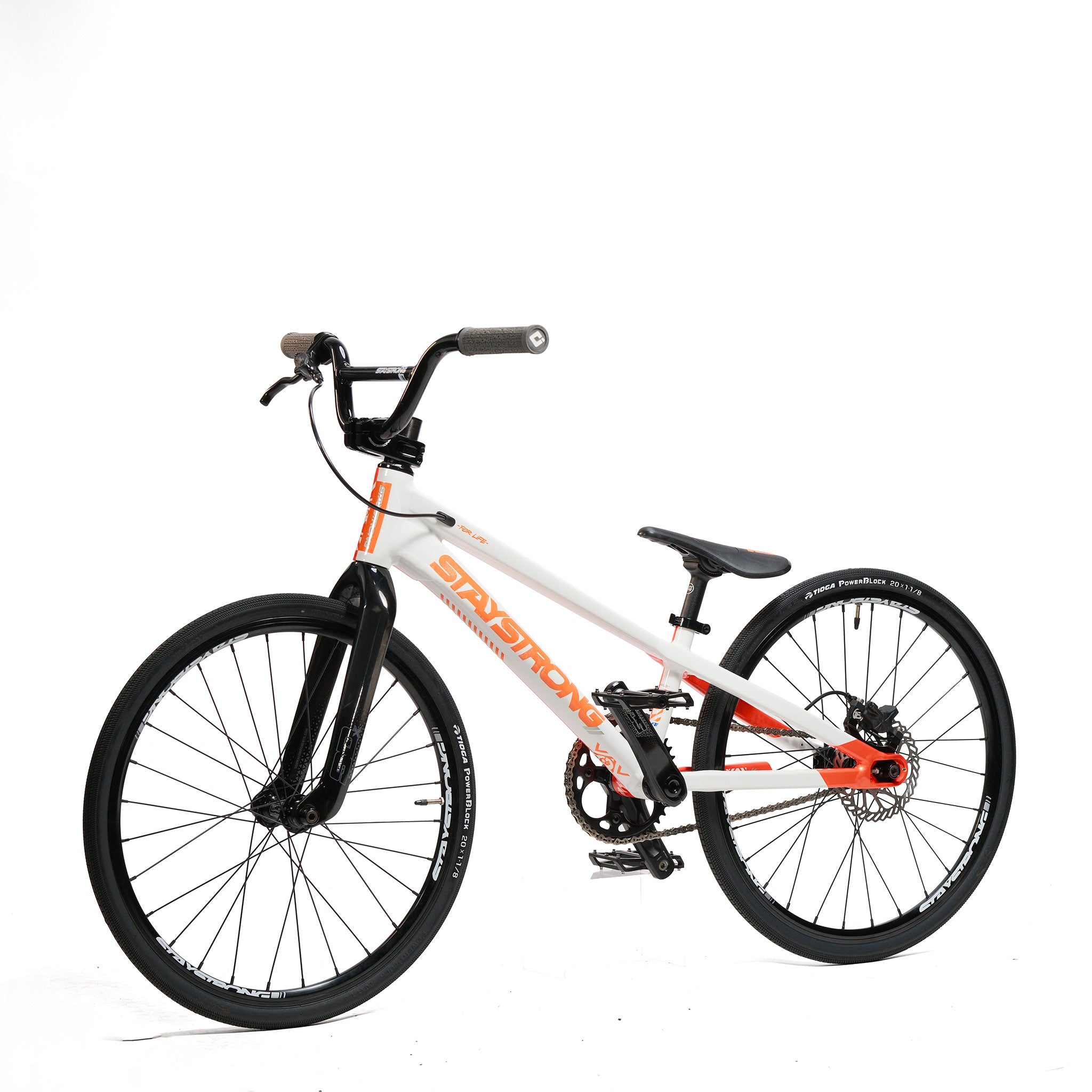 The Stay Strong V5.1 Junior Race Bike features a lightweight aluminium junior disc frame in white and orange, complemented by black wheels, flat pedals, and straight handlebars, and is displayed against a white background.