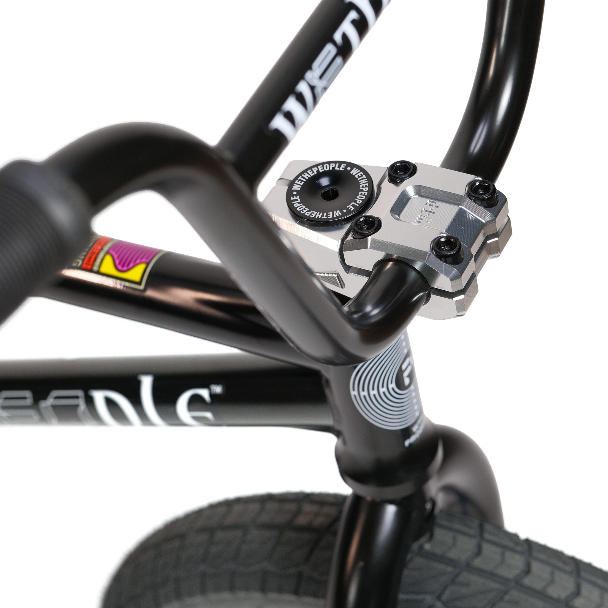 Close-up of the Wethepeople Prodi-G-Unit 18 Inch Custom Bike handlebar and stem, showcasing its parts and displaying the front wheel, grips, and stem bolts against a white background.