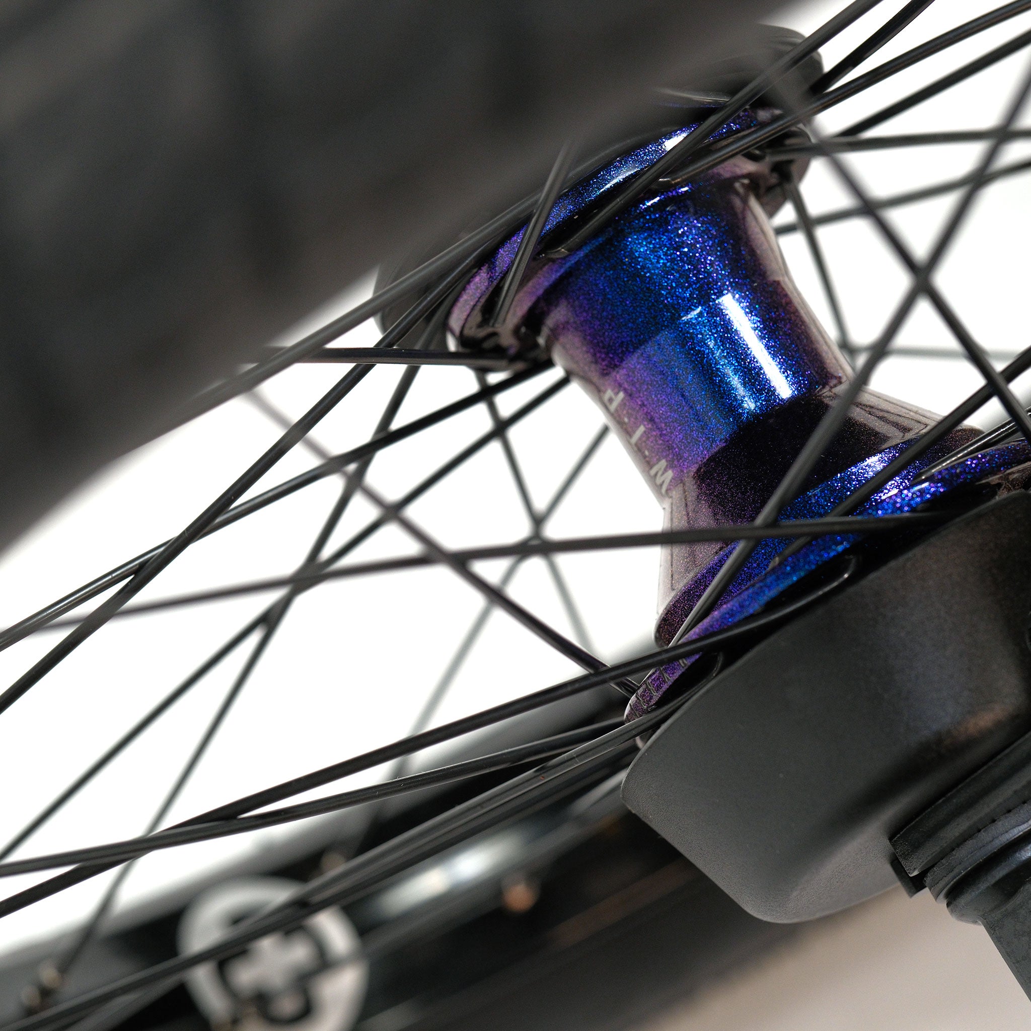 Close-up of a BMX bike wheel showing black spokes, a metallic blue hub—possibly from the Wethepeople Prodi-G-Unit 18 Inch Custom Bike—and part of a tire, featuring premium Eclat parts for added performance.
