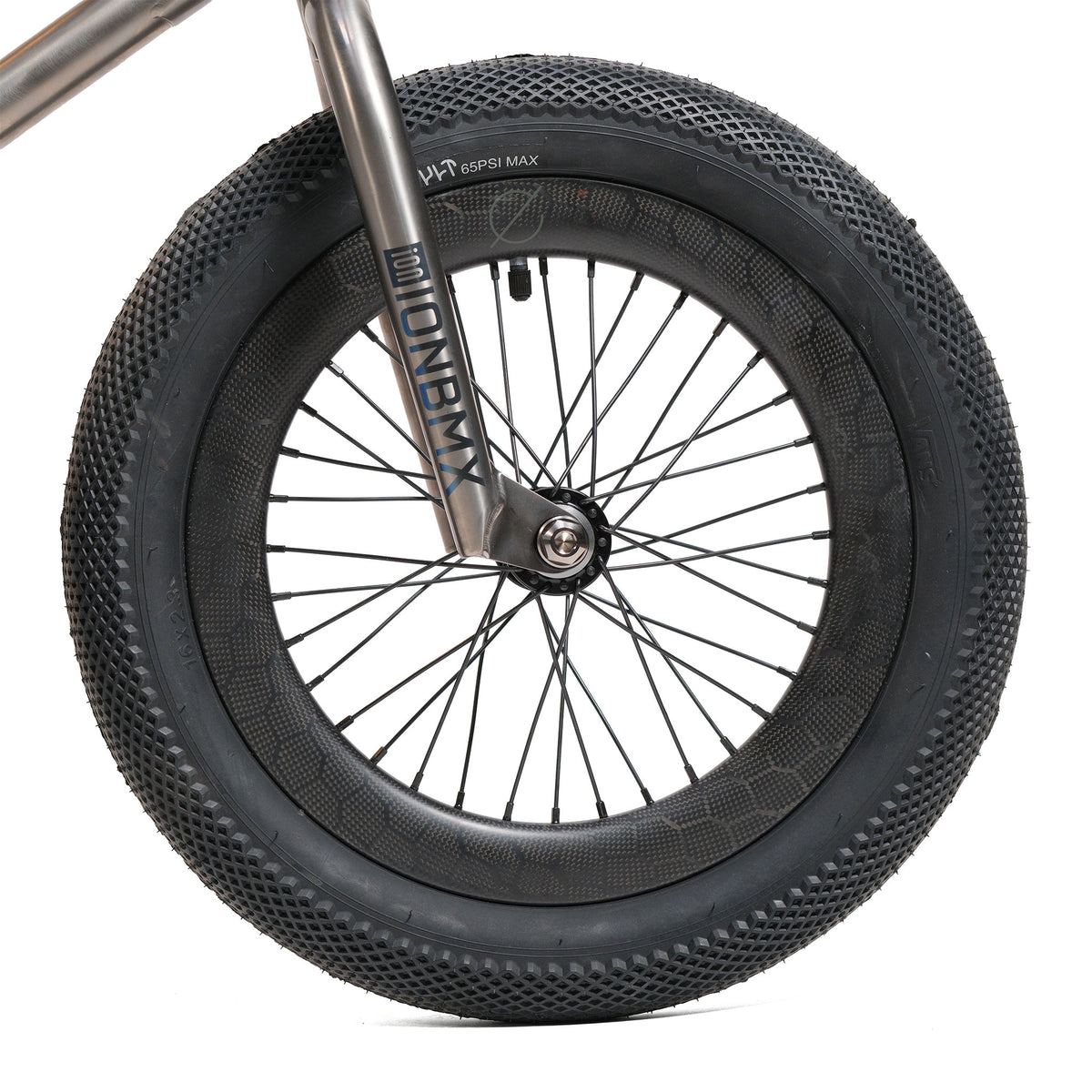 Close-up of the ION BMX Ti16 Custom Titanium 16 Inch Bike’s lightweight front wheel, featuring a thick knobby tire, black spokes, and part of the metal fork visible against a white background.