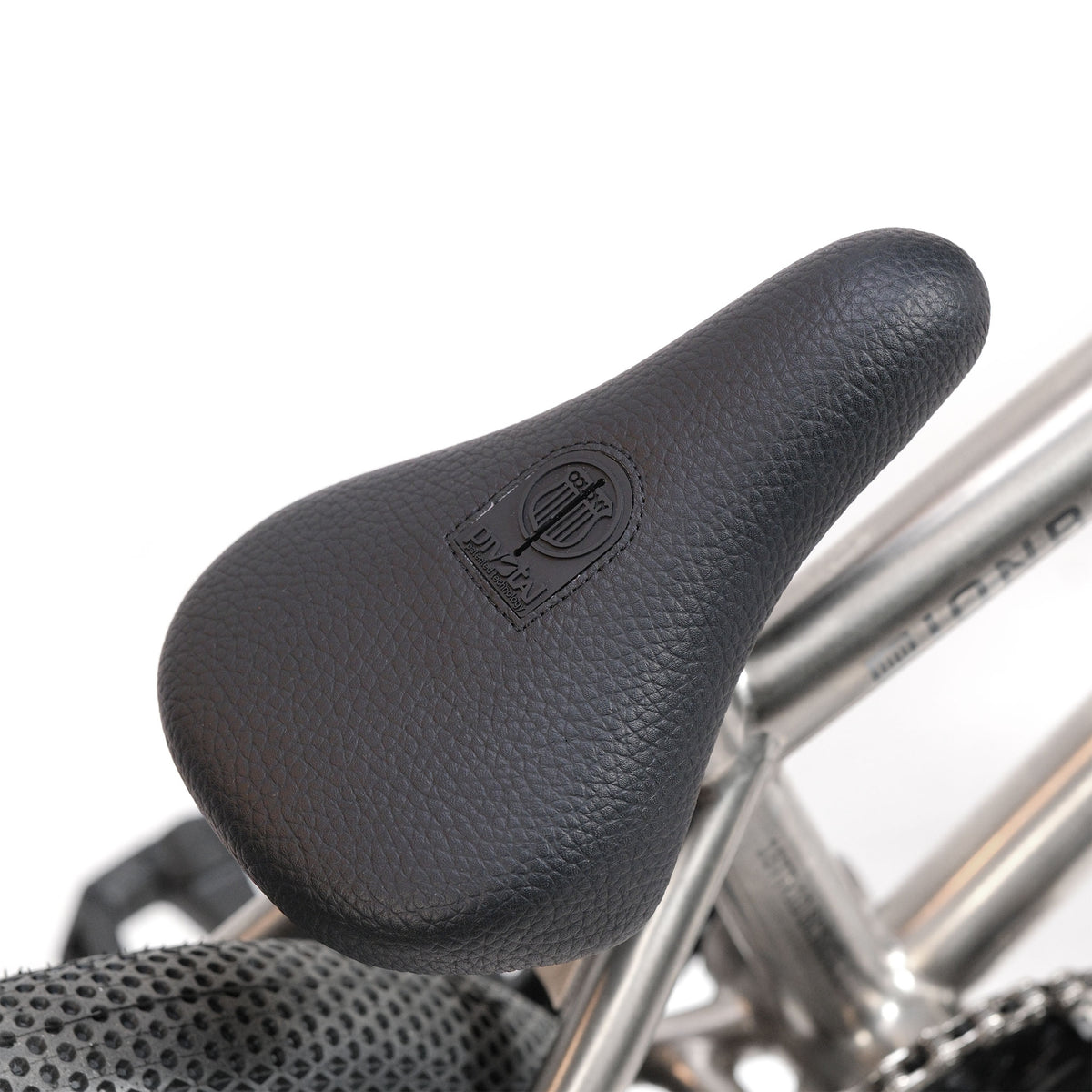 Black textured bicycle seat with an embossed logo, mounted on the ION BMX Ti16 Custom Titanium 16 Inch Bike frame. Parts of the rear wheel and chain are partially visible.