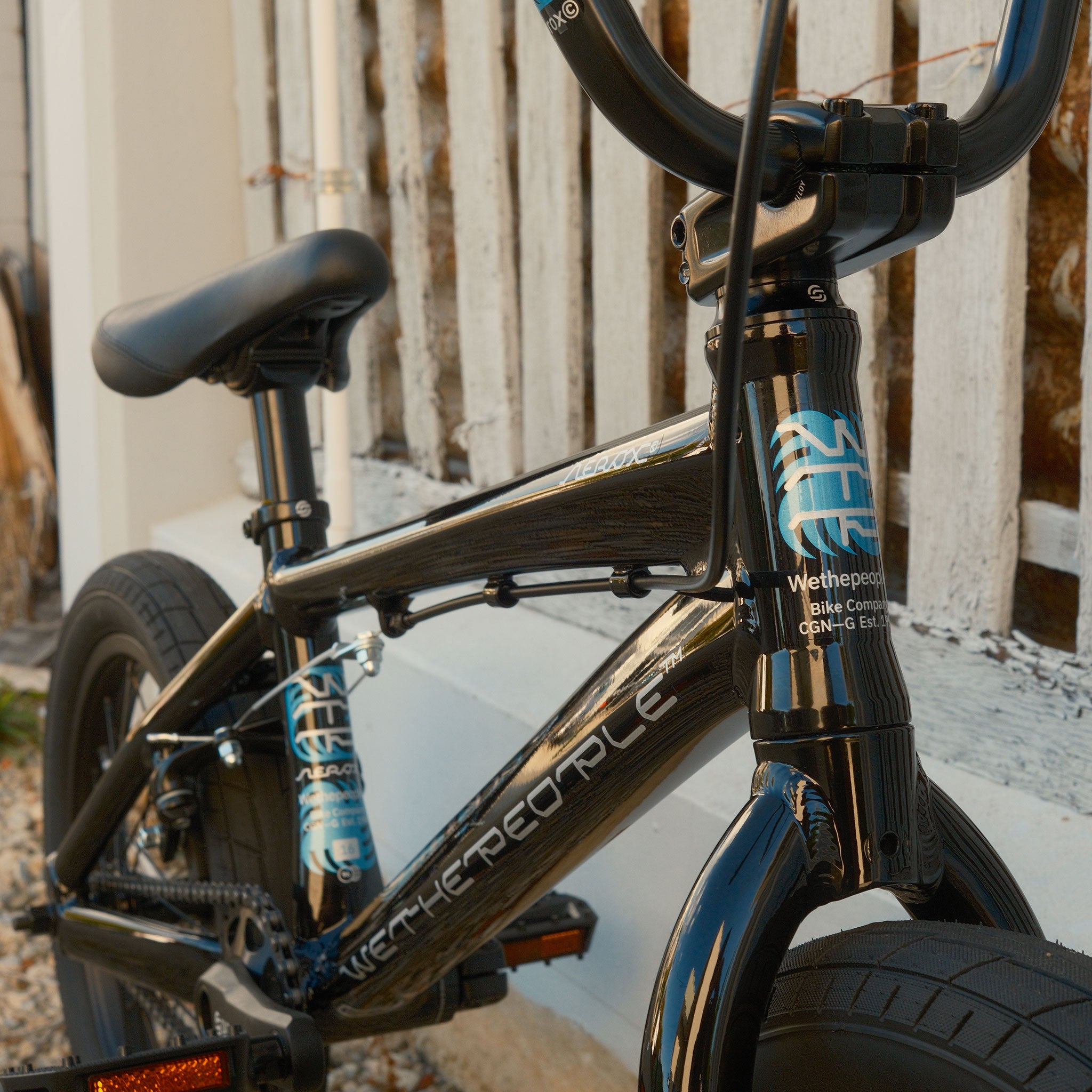 Close-up of a Wethepeople Aerox 16 Inch Bike, featuring a black lightweight alloy frame, parked beside a white wooden fence with focus on its handlebars and front wheel.