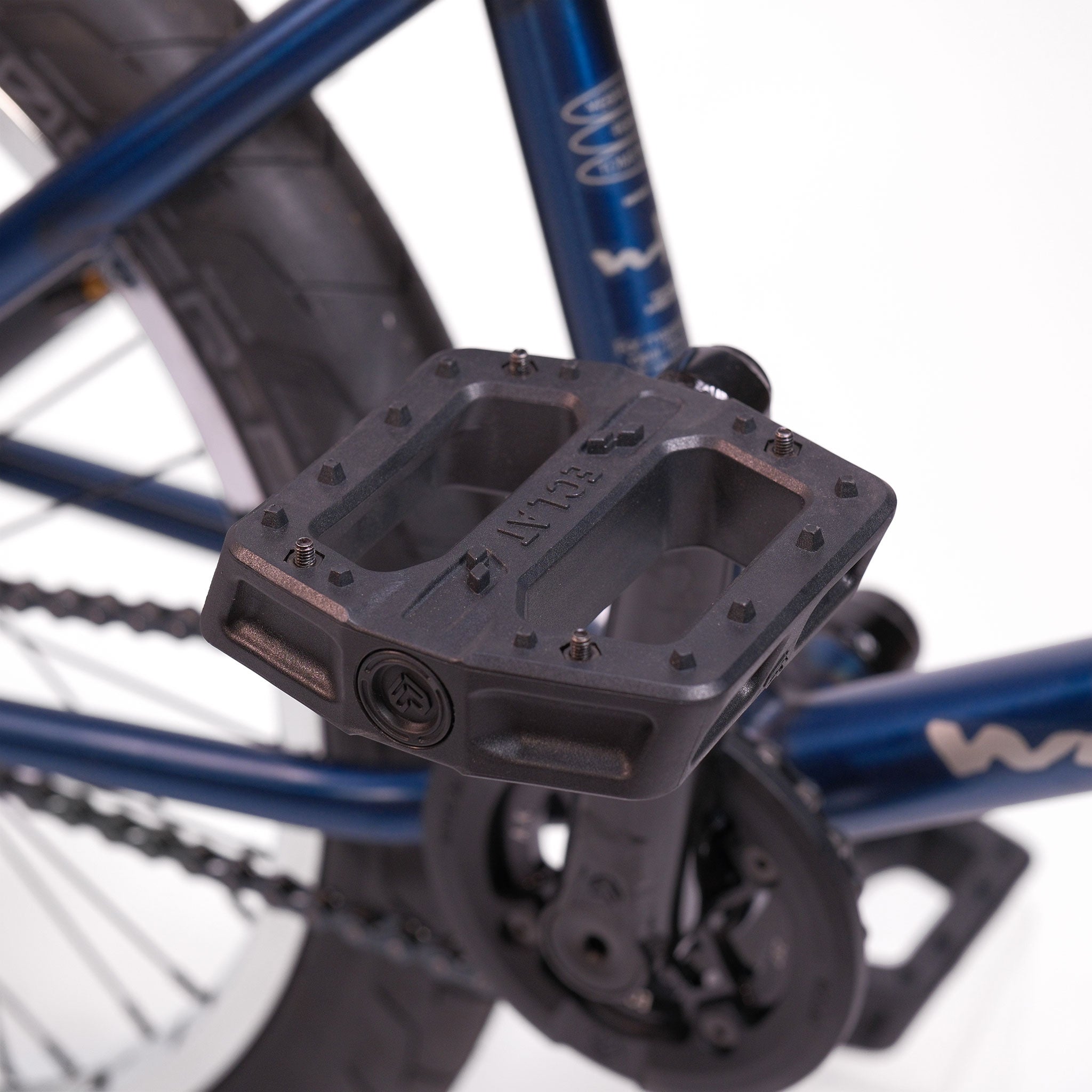Close-up of a black pedal on a blue crank arm attached to the Wethepeople Tomorrow X TA Custom build BMX bike, with the frame, chain, and rear wheel partially visible in the background.