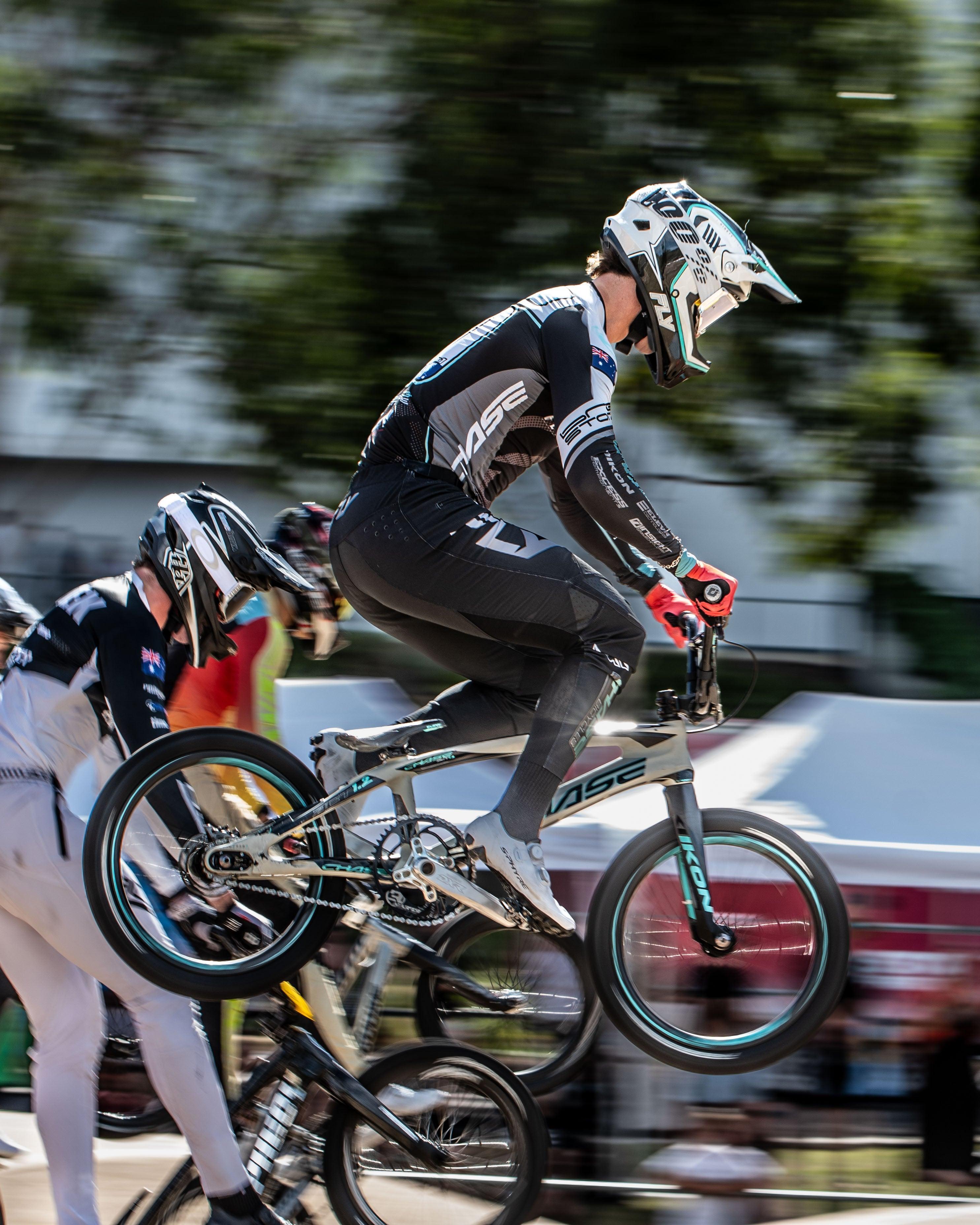 Two cyclists with helmets and racing suits jump during a BMX race at the National Championships. Capture thrilling moments like this with the LUXBMX Race Photo Package—perfect for action-packed BMX events.
