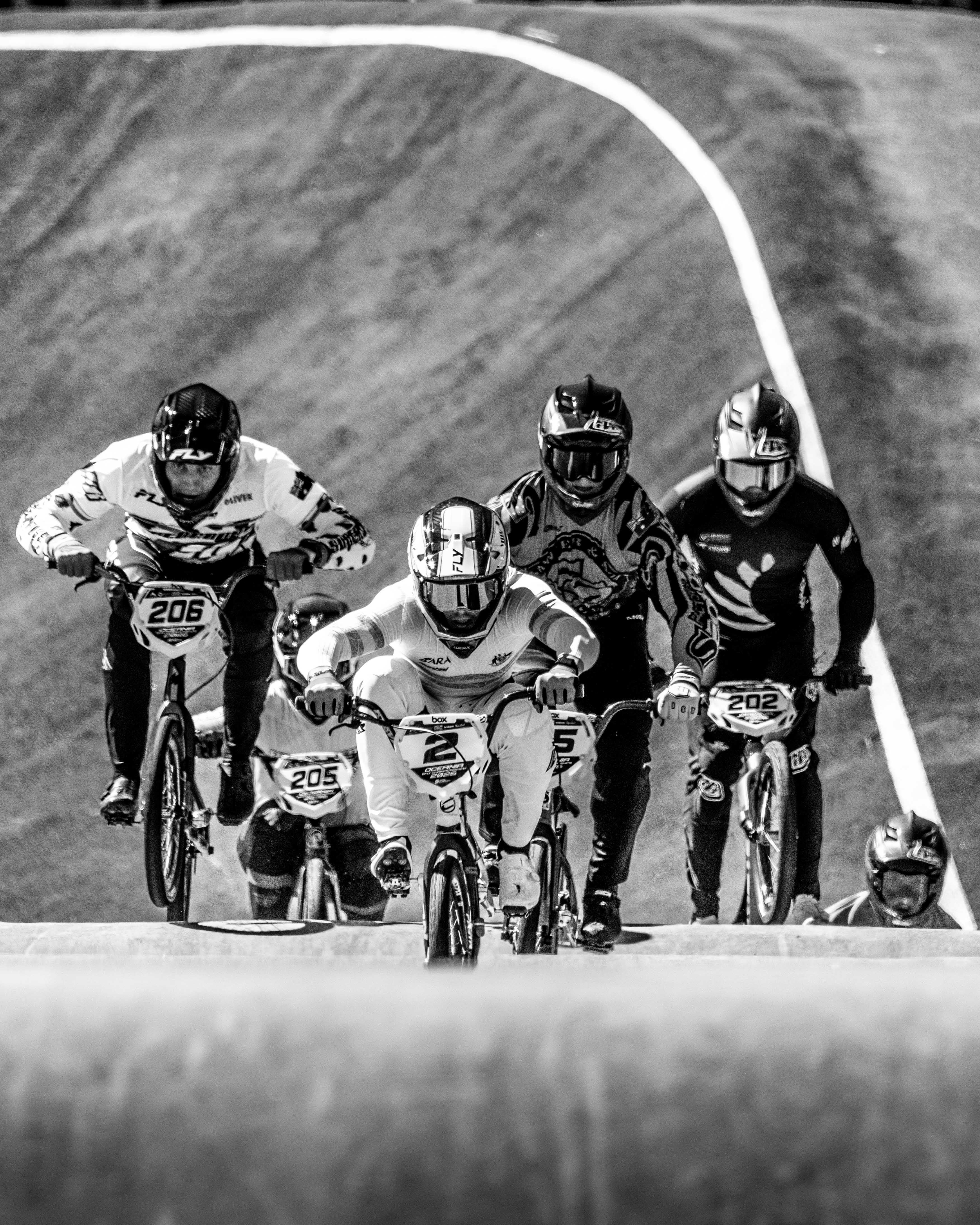 The LUXBMX Race Photo Package features five BMX cyclists at the National Championships, racing closely on a track from a dynamic low-angle view—all in helmets and numbered jerseys, with the lead rider ahead.