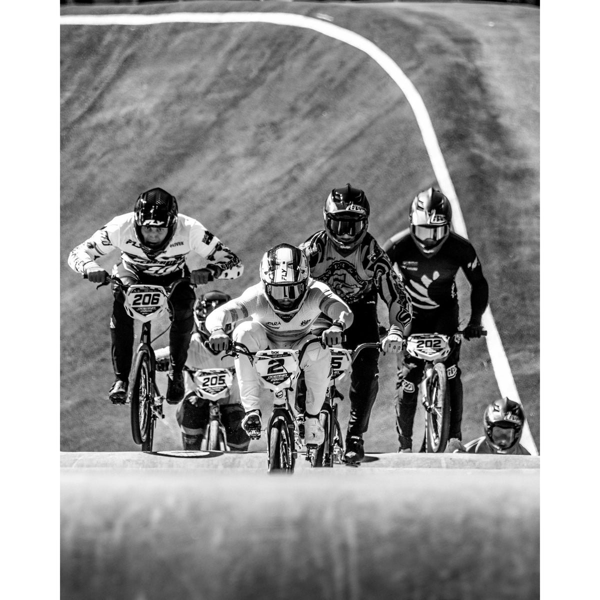 Five BMX cyclists race up a hill on a dirt track—captured in dramatic black and white, each rider wearing helmets and numbered jerseys—in this striking LUXBMX NSW State Championship’s 2026 Photo Packages - Lake Mac image, exemplifying dynamic race photography.
