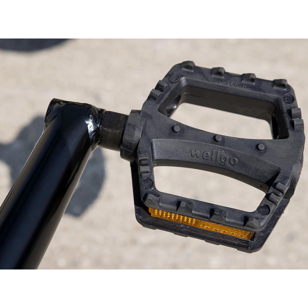 Close-up of a black "wellgo" pedal with a yellow reflector, attached to a black crank arm on light concrete—perfect for pro-level setups like the 2025 Sunday Primer 16 Inch Bike.