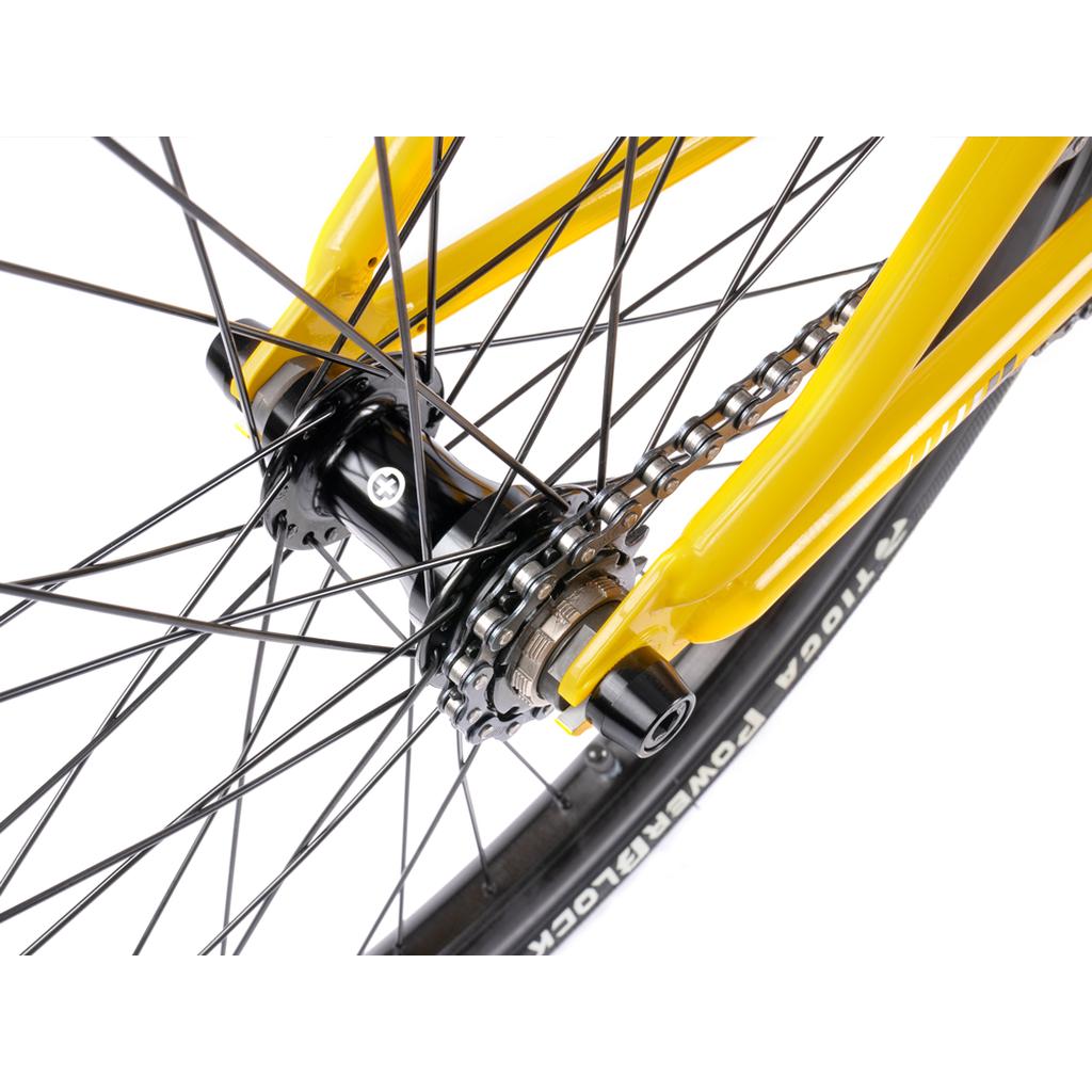 Close-up of the rear wheel on a yellow Wethepeople Atlas 24 Inch Bike, highlighting the spokes, chain, hub, and a section of the 24" tire.