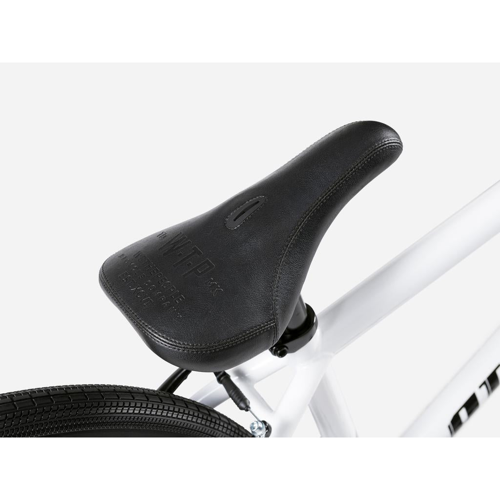 Close-up of a black bicycle seat mounted on the Wethepeople Atlas 24 Inch Bike's white frame, featuring textured details and embossed branding—ideal for cruiser bikes with 24" wheels.
