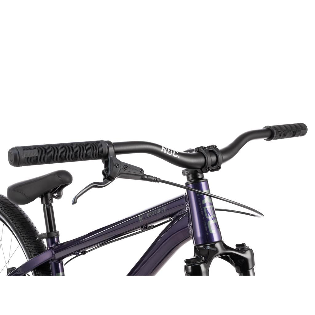 Close-up of a black handlebar with grips, brake lever, and front brake cable attached to the purple frame of the Radio Griffin 26 Inch Bike.