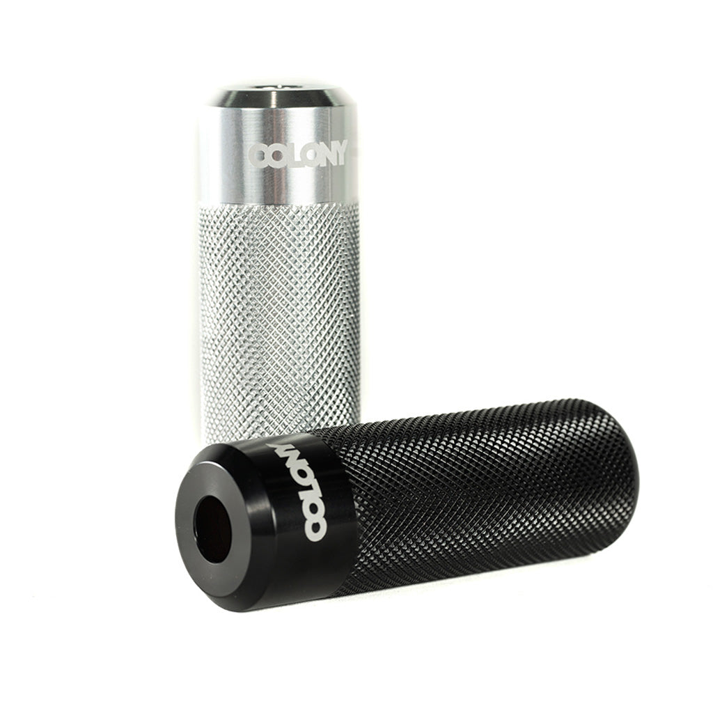 A pair of high-quality black and silver Colony Jam Circle Flatland Pegs on a white background.