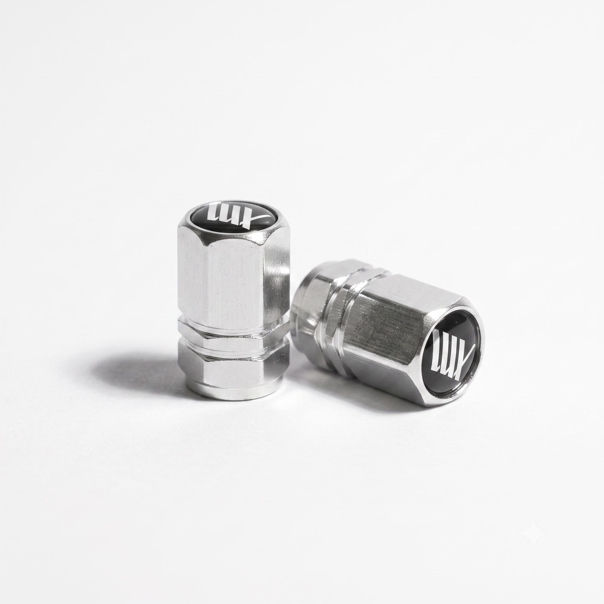 The LUXBMX Hex Logo Alloy Valve Cap (Pair) features two silver hexagonal alloy caps with a black and white "LUX" logo, perfect as stylish bike accessories, shown on a white background.