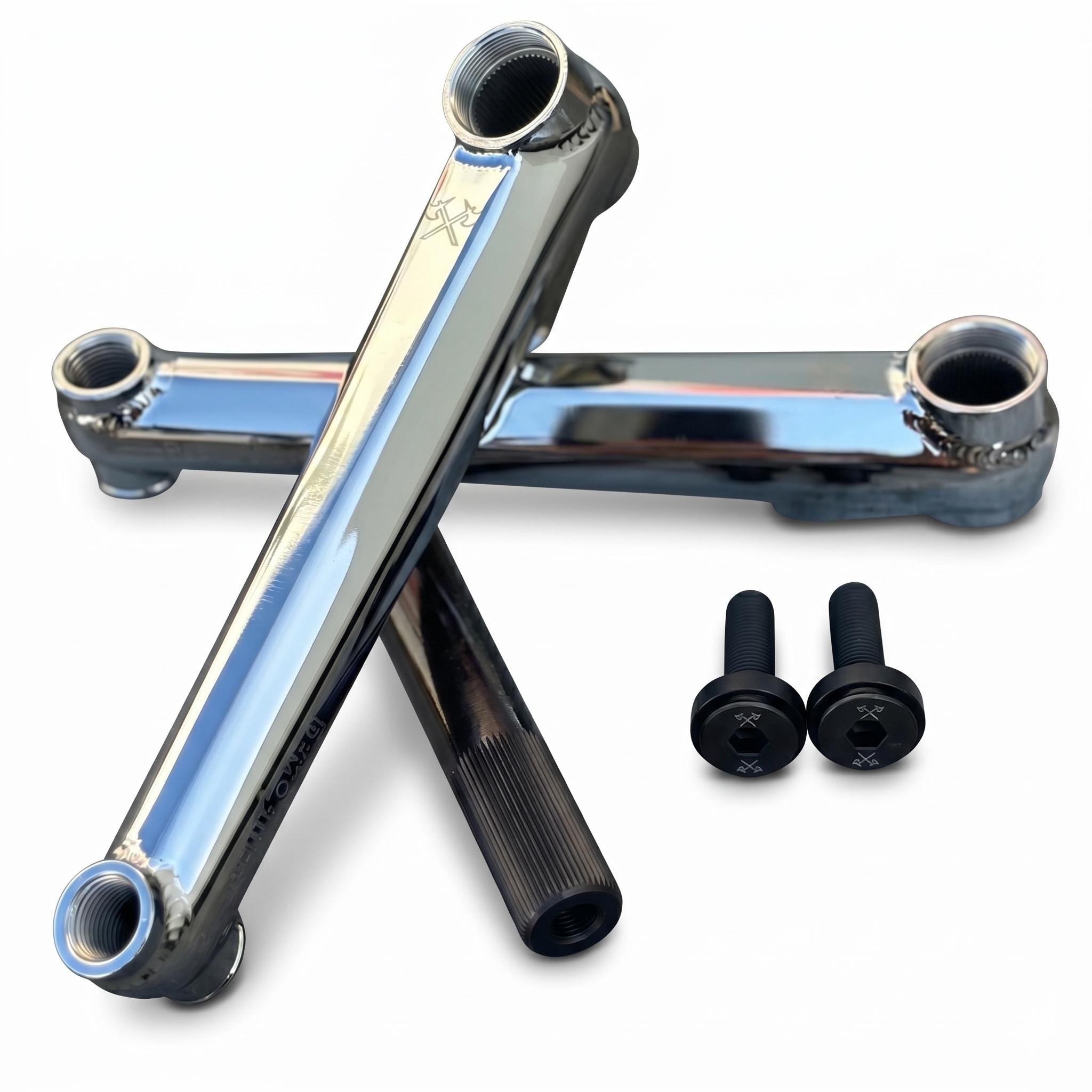 Two Demolition Revolt Cranks in metallic finish are crossed over each other beside two black bolts with a strong chromoly spindle, all displayed on a white background.