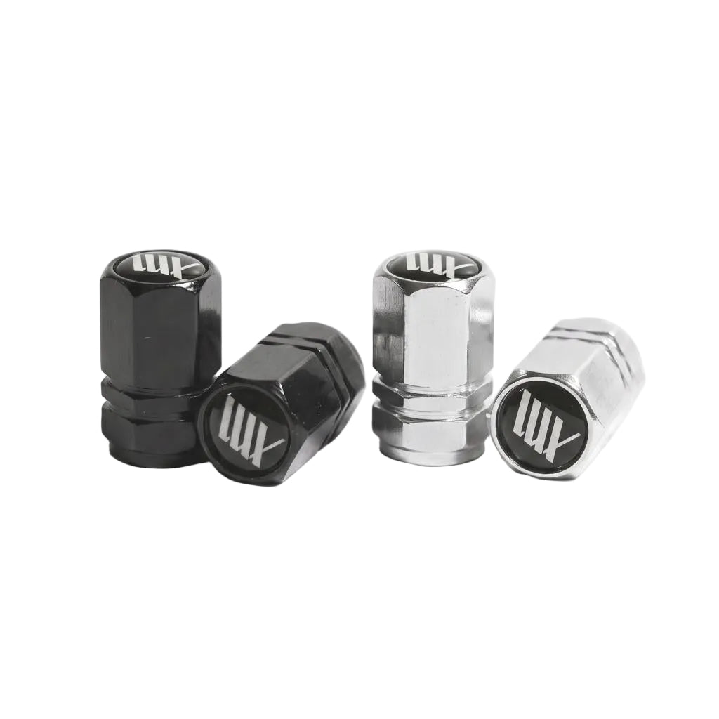 Two pairs of LUXBMX Hex Logo Alloy Valve Caps—one black, one silver—are displayed on a white surface, each showcasing the signature "LUX" logo found on premium LUXBMX accessories.