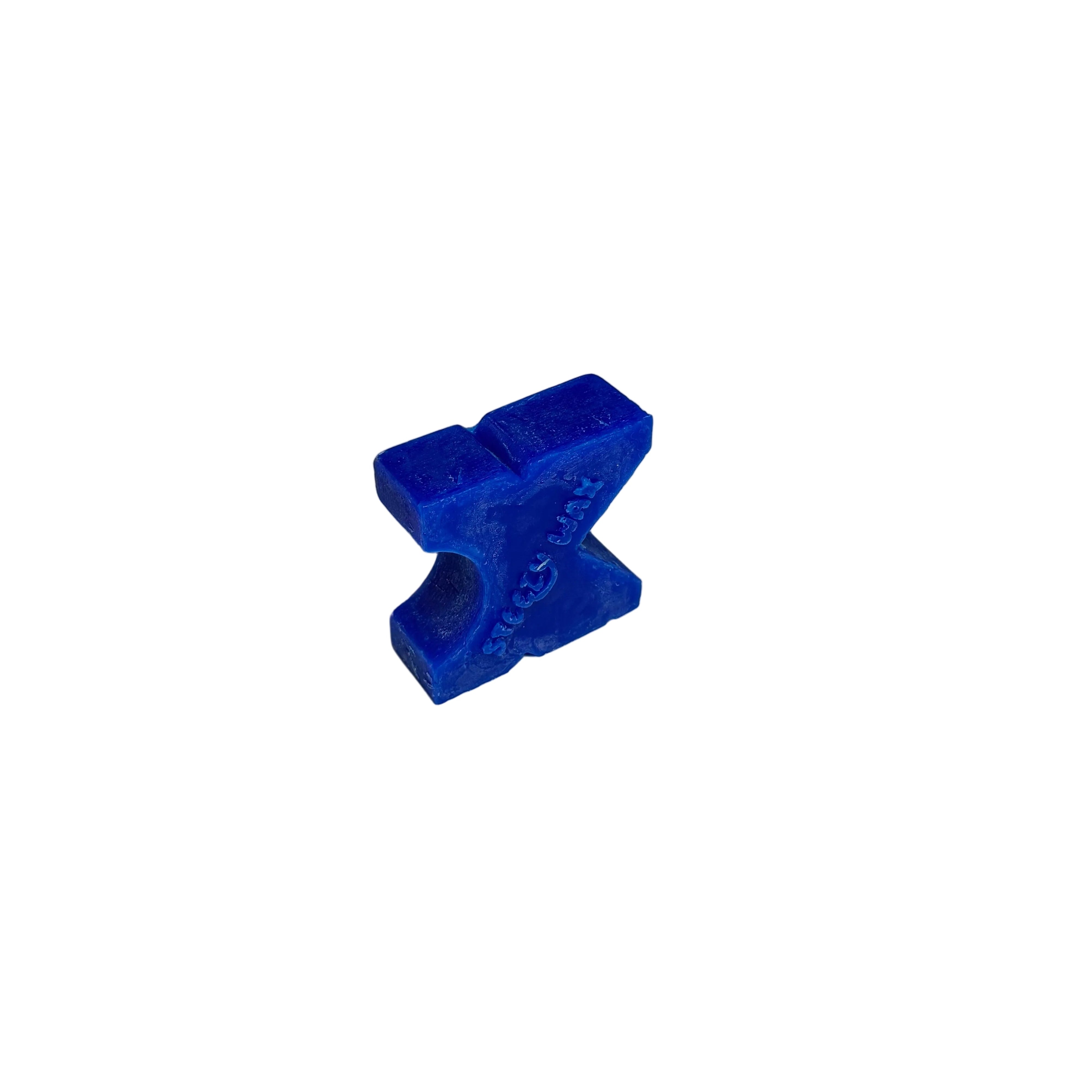 A small, blue, X-shaped Steezy Wax / K-Slide skate wax sits on a plain white surface against a neutral background.