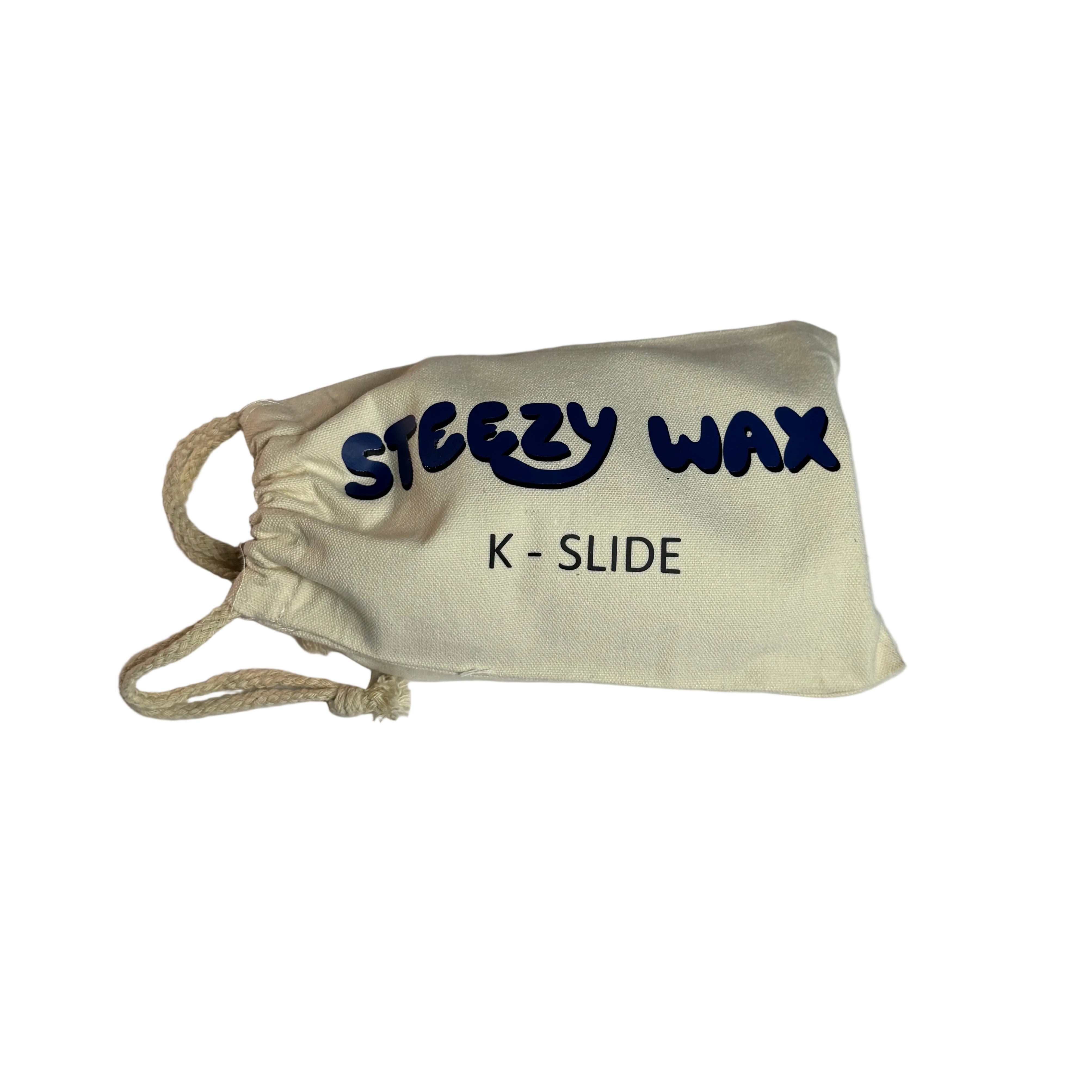 A small drawstring pouch labeled "Steezy Wax / K-Slide" rests on a white surface, holding a premium skate wax block from Australia.