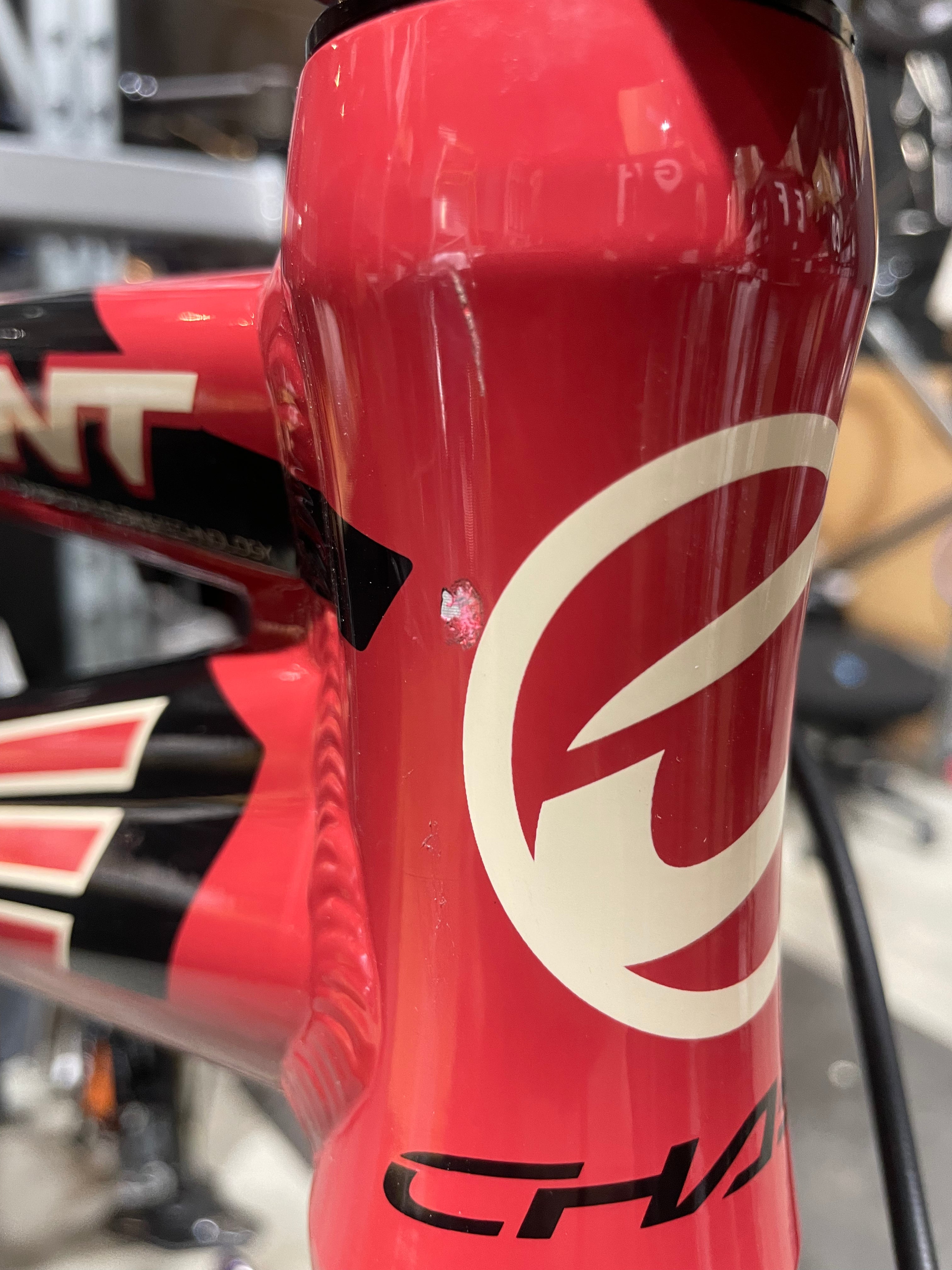 Close-up of a red Chase Element Pro XXXL Bike *scratch and dent* frame showing a noticeable paint chip with visible white underlayer near the white logo, black design accents, and Ikon carbon forks.