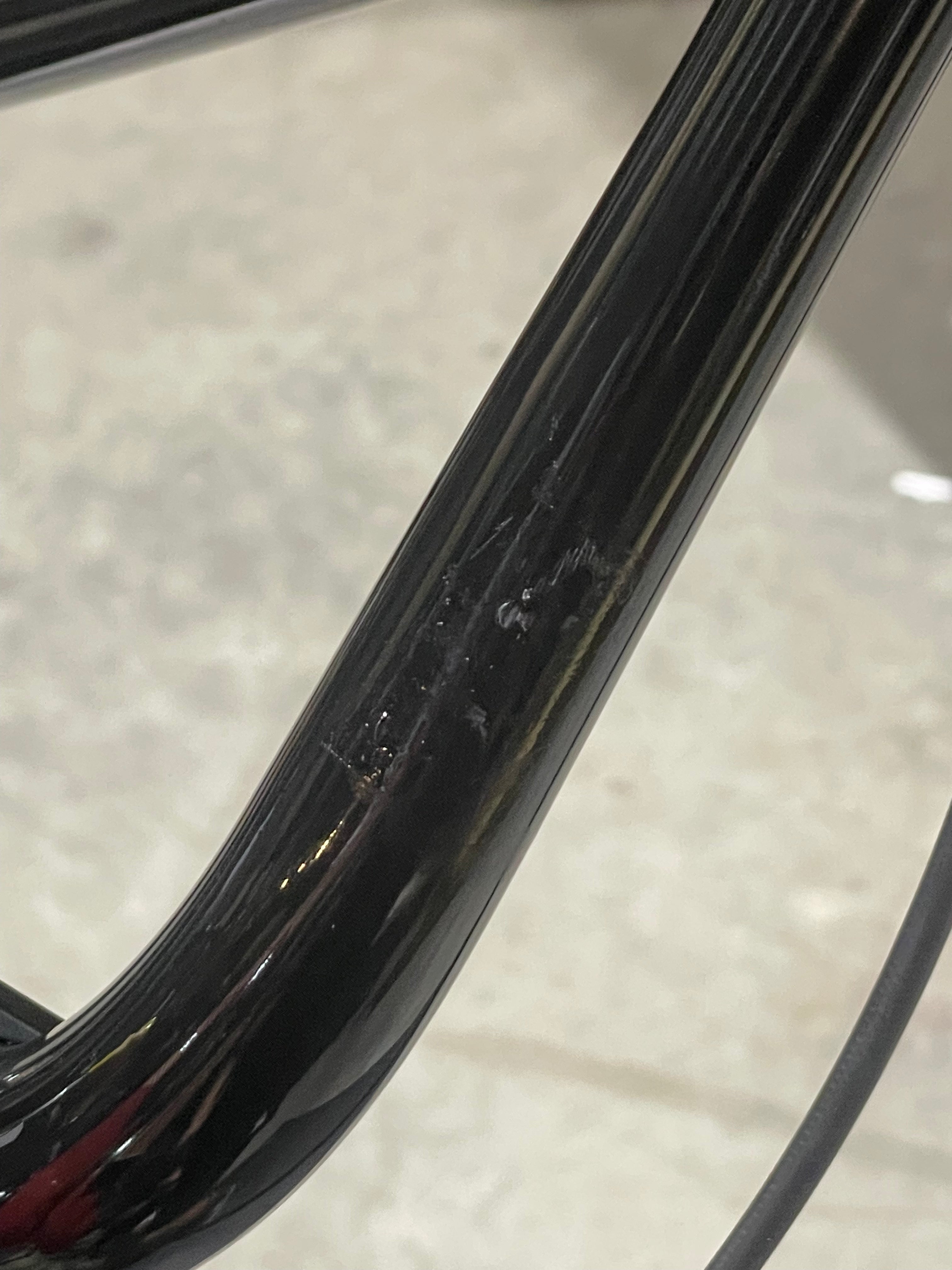 Close-up of a black metal tube with visible scuffs and scratches, likely part of a Chase Element Pro XXXL Bike *scratch and dent*, set against a blurred gray background.