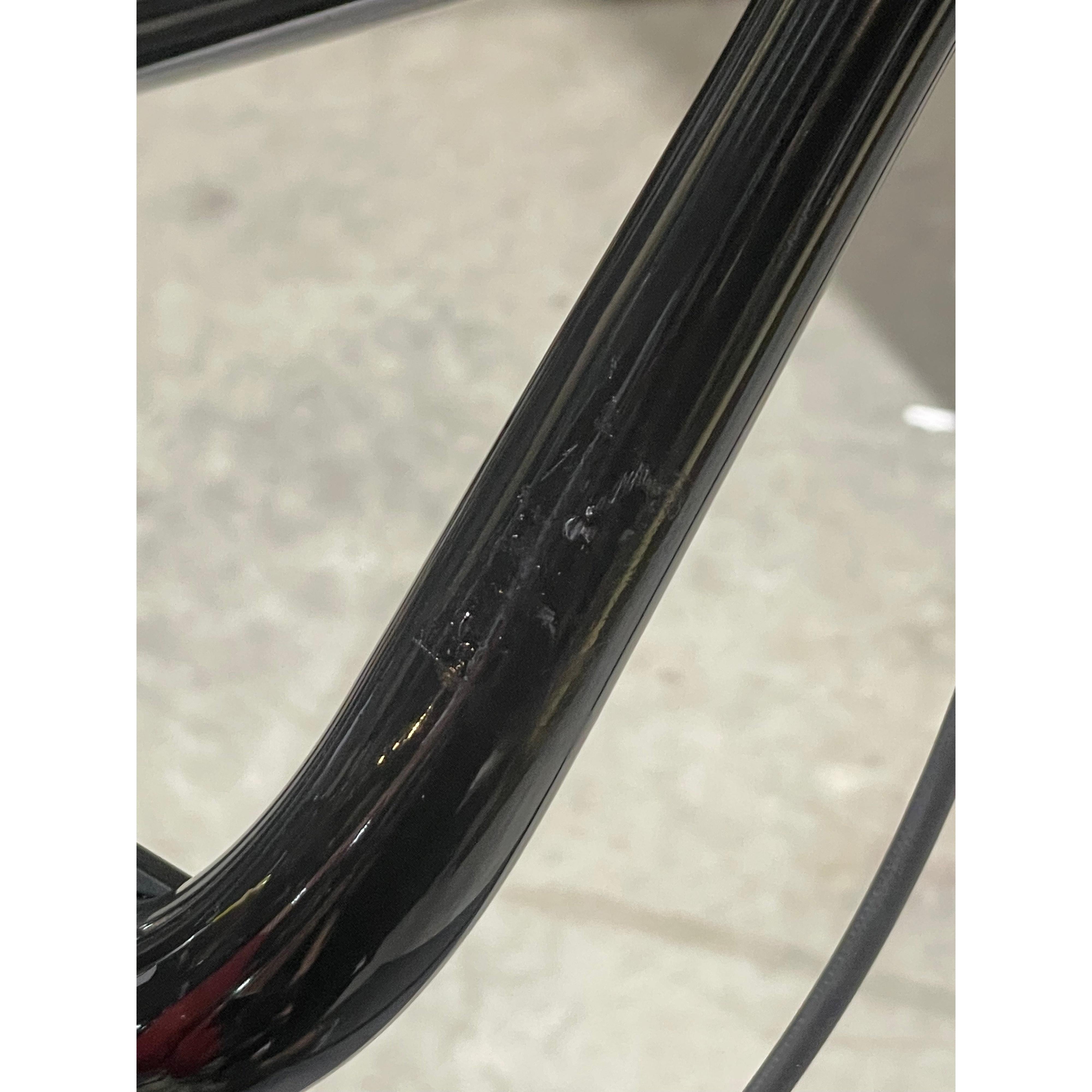 Close-up of a black metal tube with visible scuffs and scratches, likely part of a Chase Element Pro XXXL Bike *scratch and dent*, set against a blurred gray background.