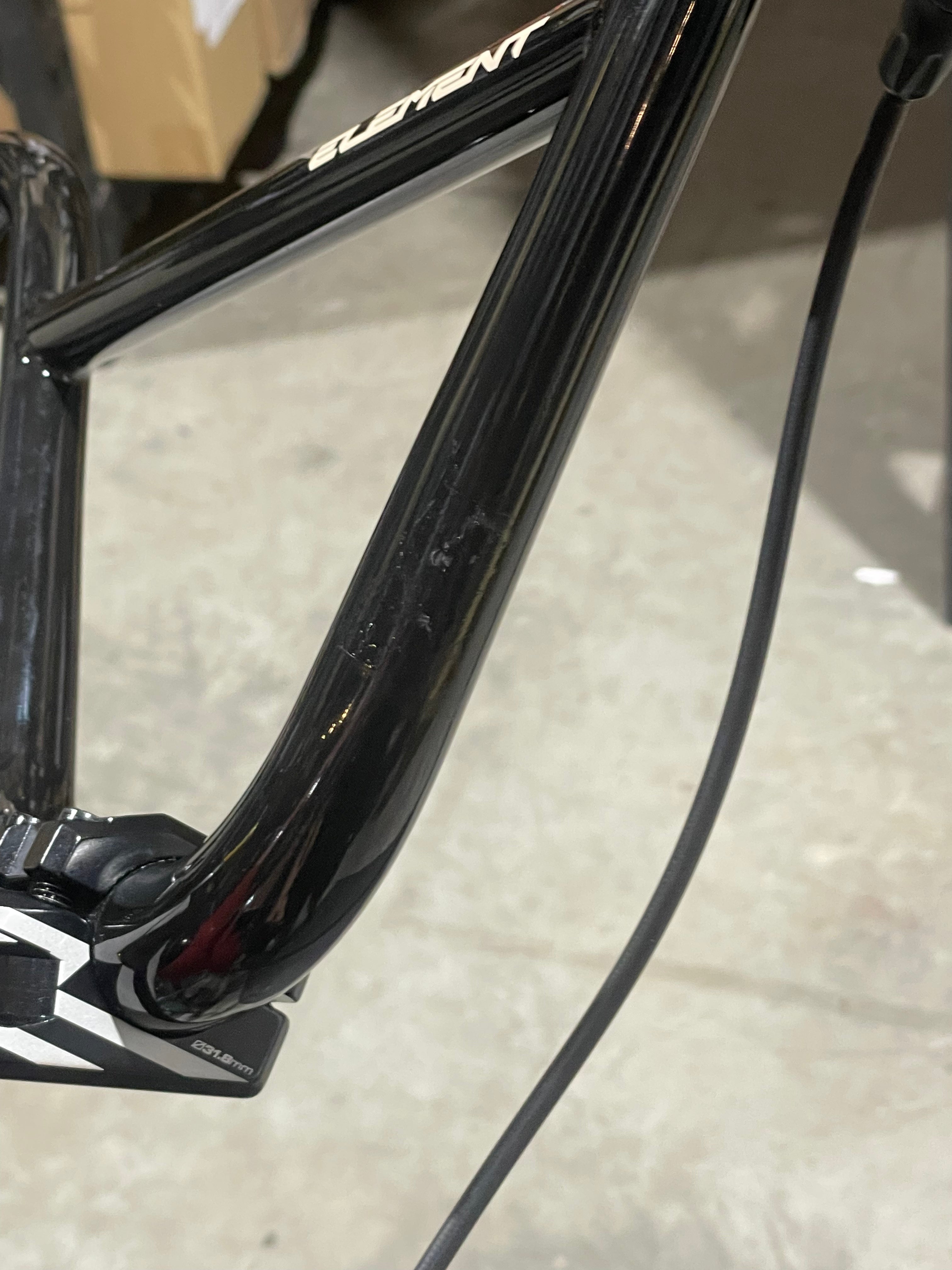 Close-up of a black Chase Element Pro XXXL Bike *scratch and dent* frame, showing visible cables and part of the handlebar stem, photographed indoors on a concrete floor.