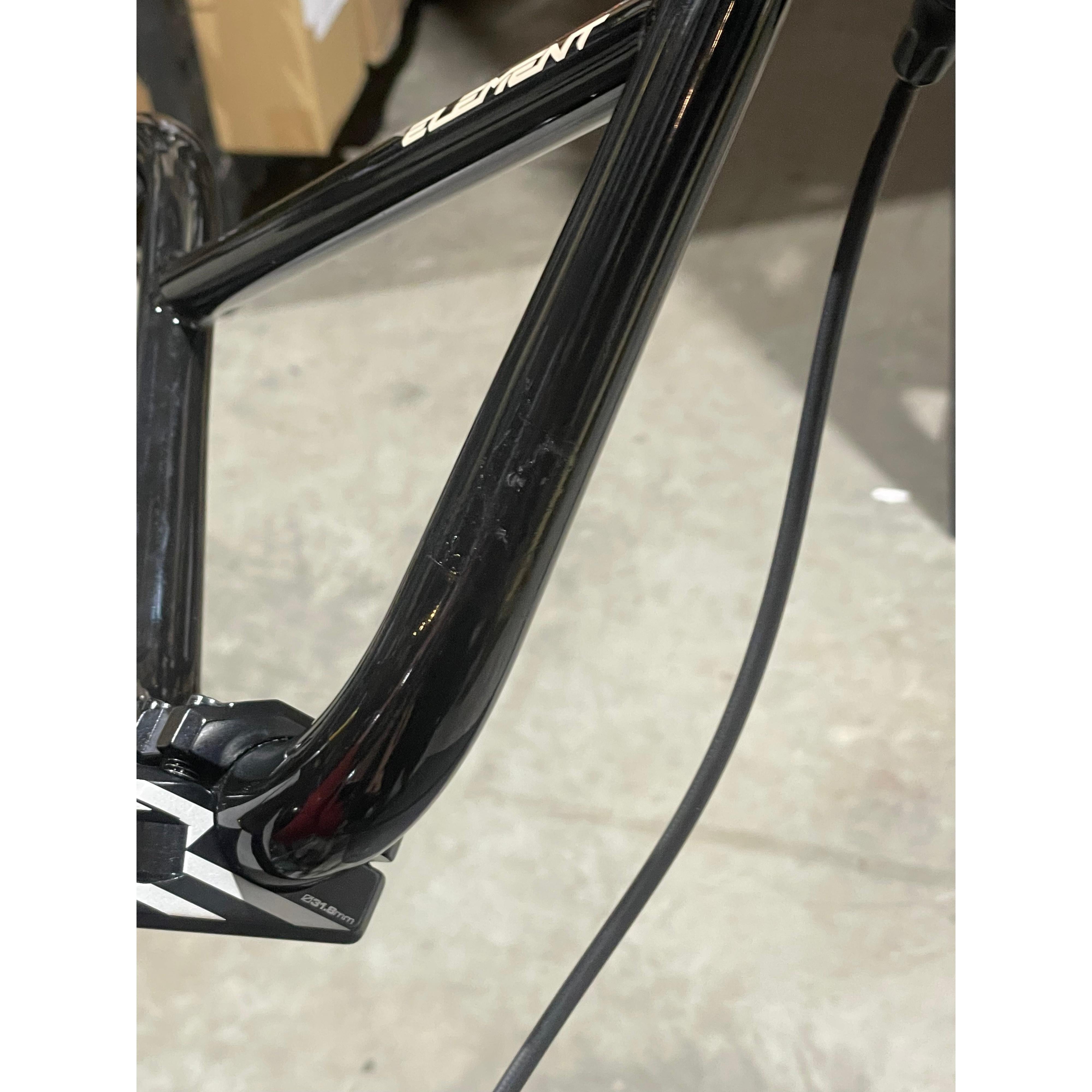 Close-up of a black Chase Element Pro XXXL Bike *scratch and dent* frame, showing visible cables and part of the handlebar stem, photographed indoors on a concrete floor.