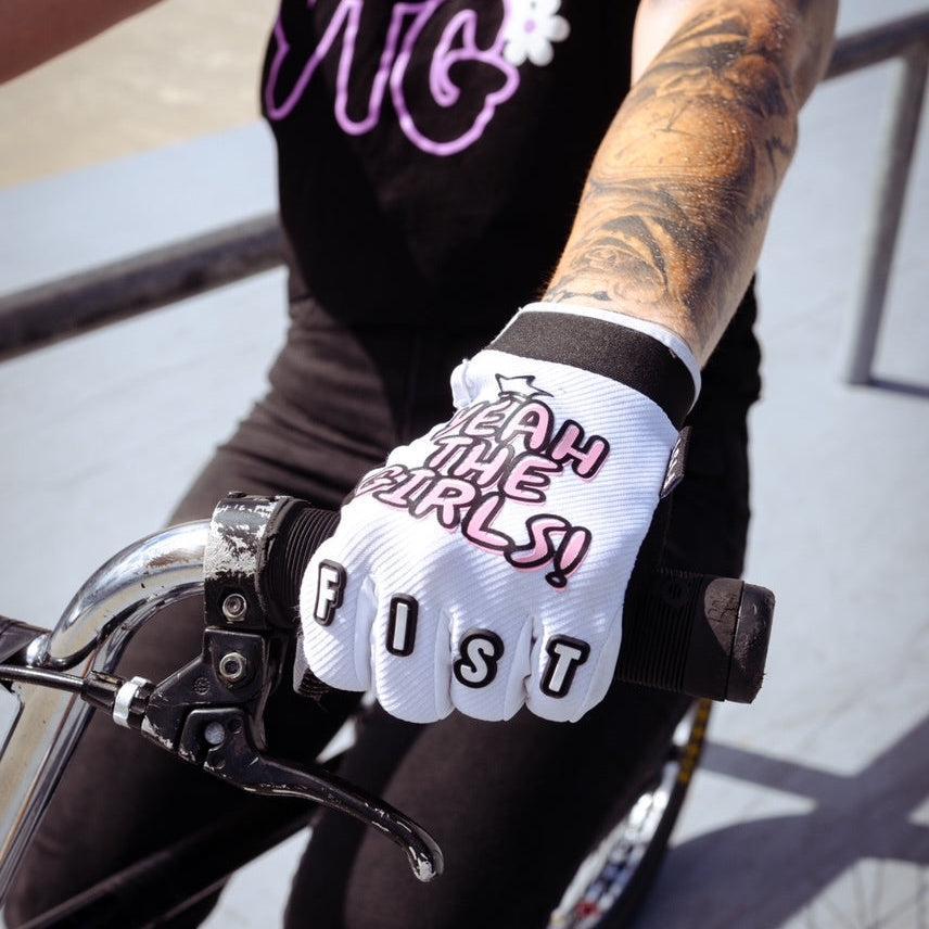 A tattooed rider grips handlebars, wearing YTG x Fist Lil' Fist Gloves—bold BMX gloves featuring "YEAH THE GIRLS!" and "FIST" in striking lettering.