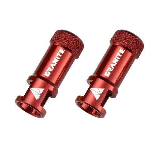 A pair of Granite Juicy CNC Presta valve caps in red anodized metal, featuring textured grip tops, diamond-shaped white logos, and bold “GRANITE” branding—these essential bike accessories also include a built-in valve core remover for added convenience.