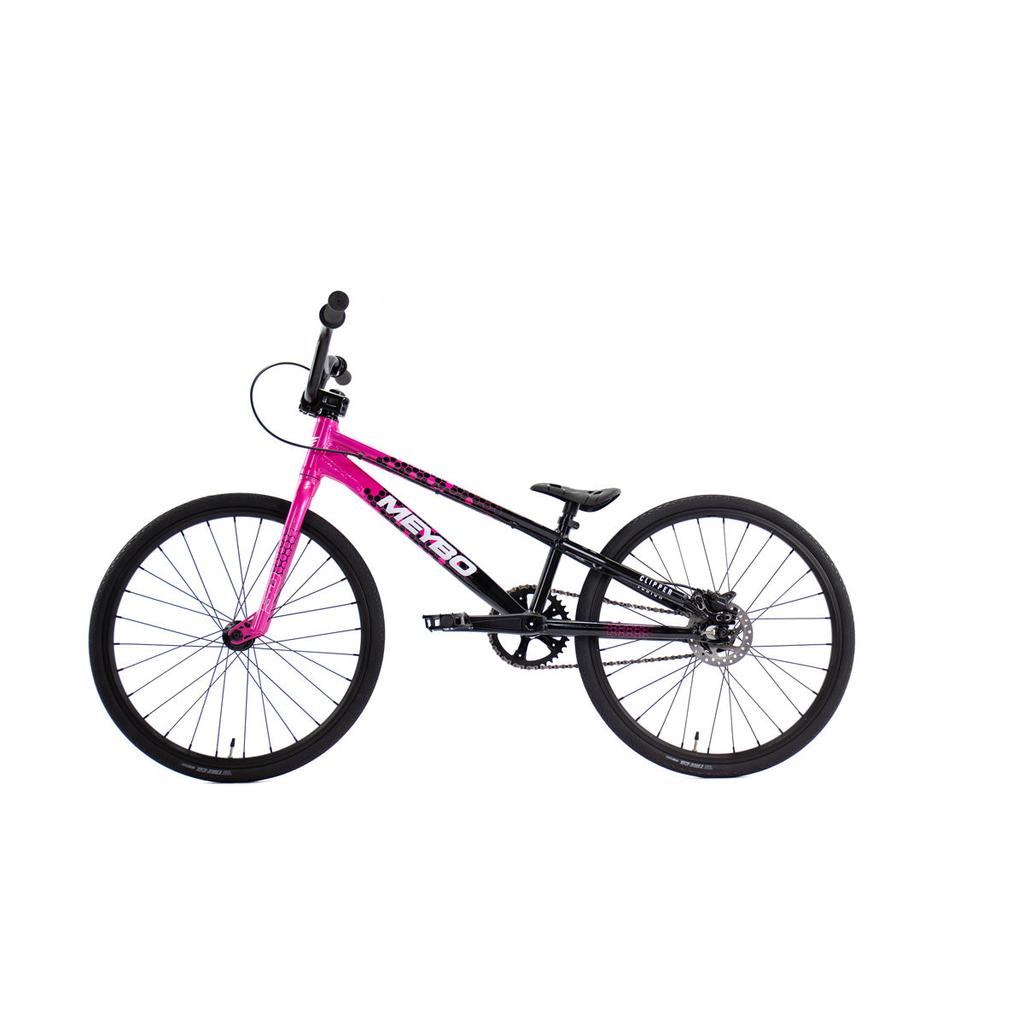 The Meybo 2026 Clipper Junior Bike is an entry-level BMX race bike with a pink front frame, black rear frame, and sleek black wheels, handlebars, and seat. Shown in profile view on a white background.