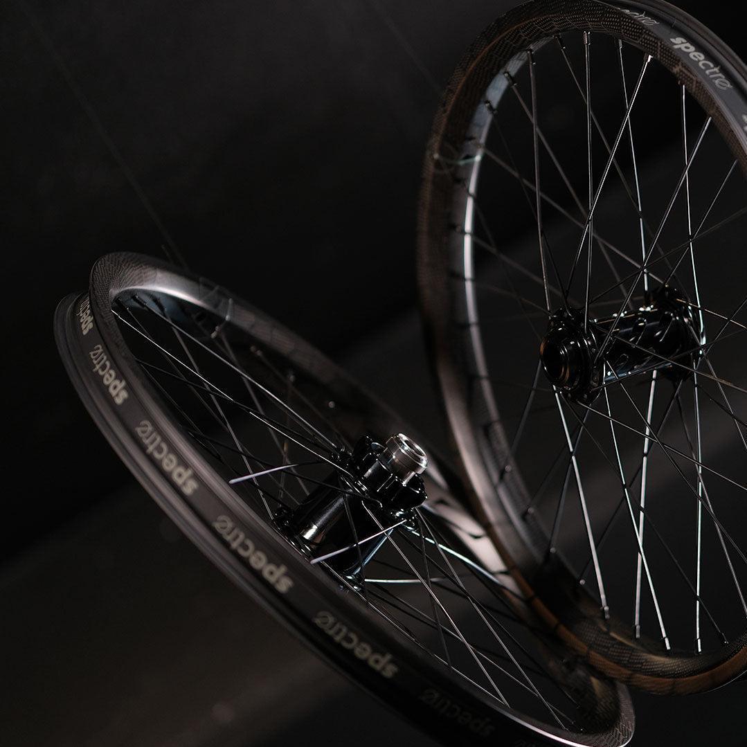 Two lightweight BMX wheels, the Spectre NME X Onyx Elite 20 Inch Disc Wheel Set (20mm/15mm), are suspended in mid-air against a dark background.
