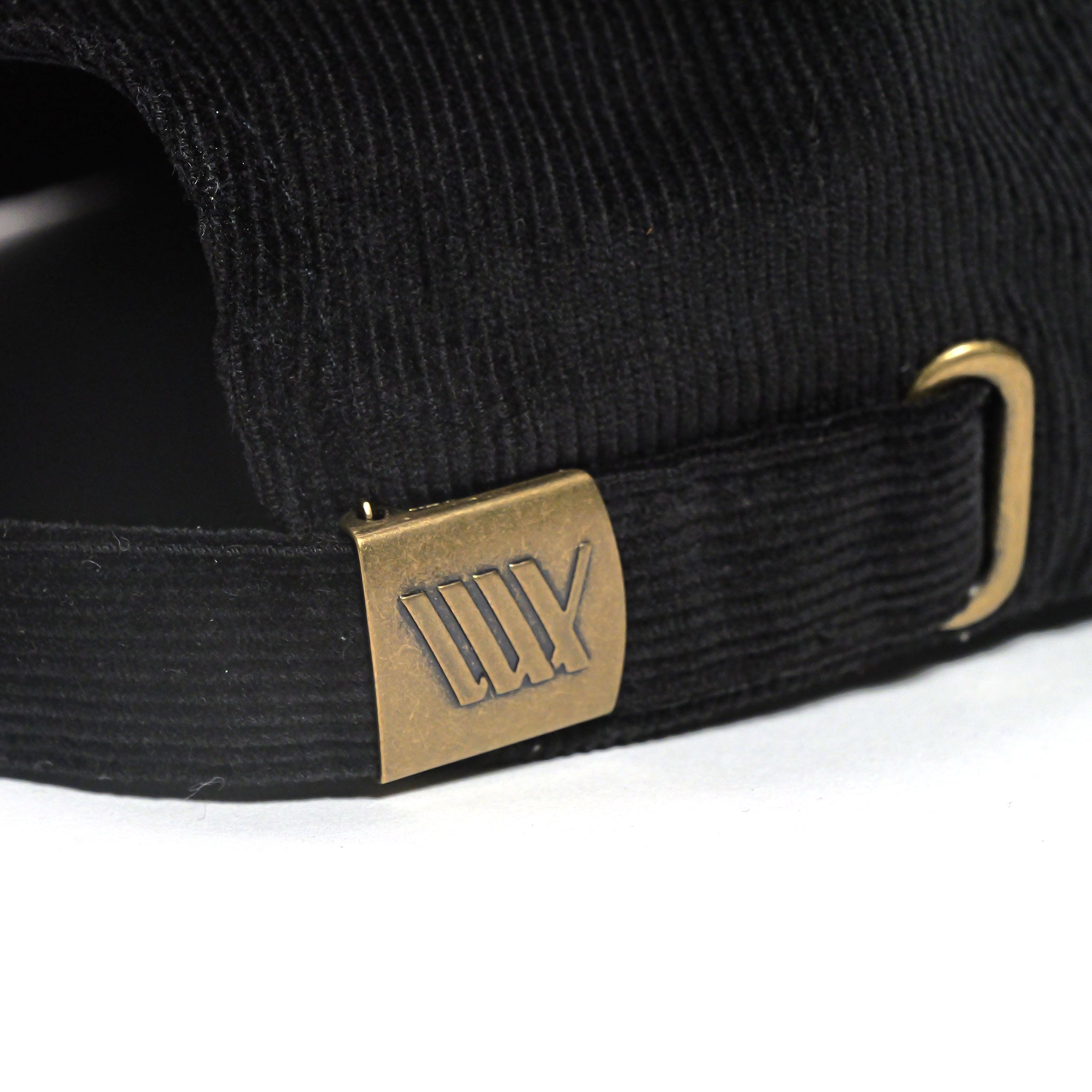 Close-up of the adjustable strap and brass buckle on the back of the LUXBMX Outfield Cap Black, featuring black cotton corduroy and an embroidered LUX logo with four vertical lines.