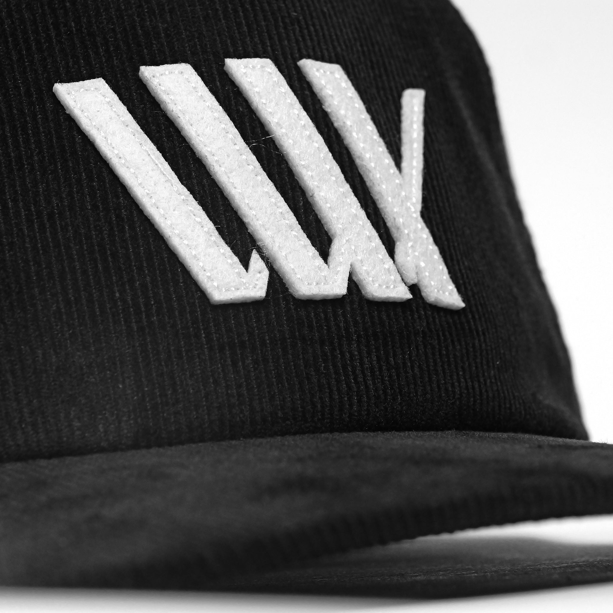 A close-up of the LUXBMX Outfield Cap Black, made from cotton corduroy with a white embroidered LUX logo and five diagonal lines on the front.