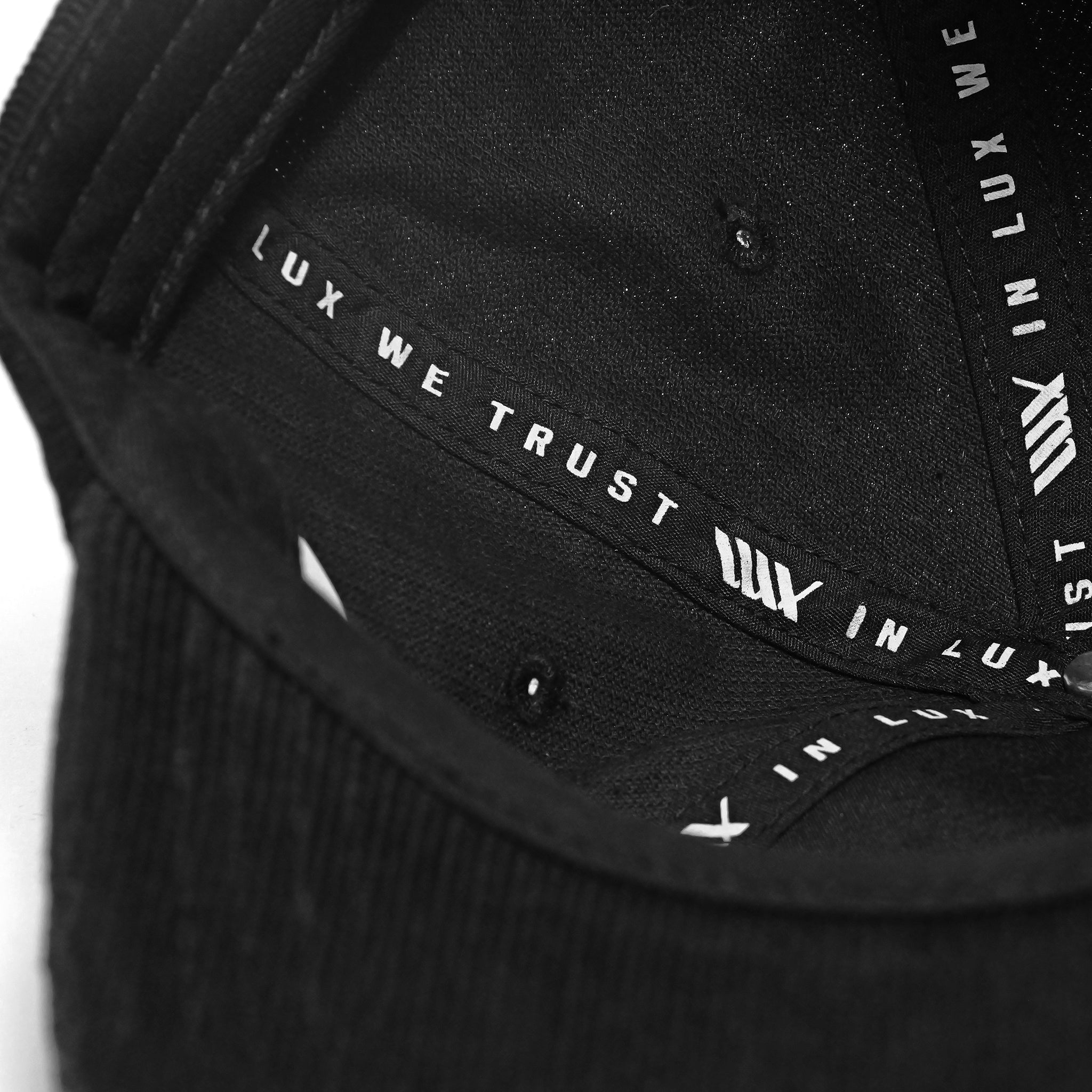 Close-up view of the LUXBMX Outfield Cap Black, made from cotton corduroy, with "IN LUX WE TRUST" printed on the inner brim lining.